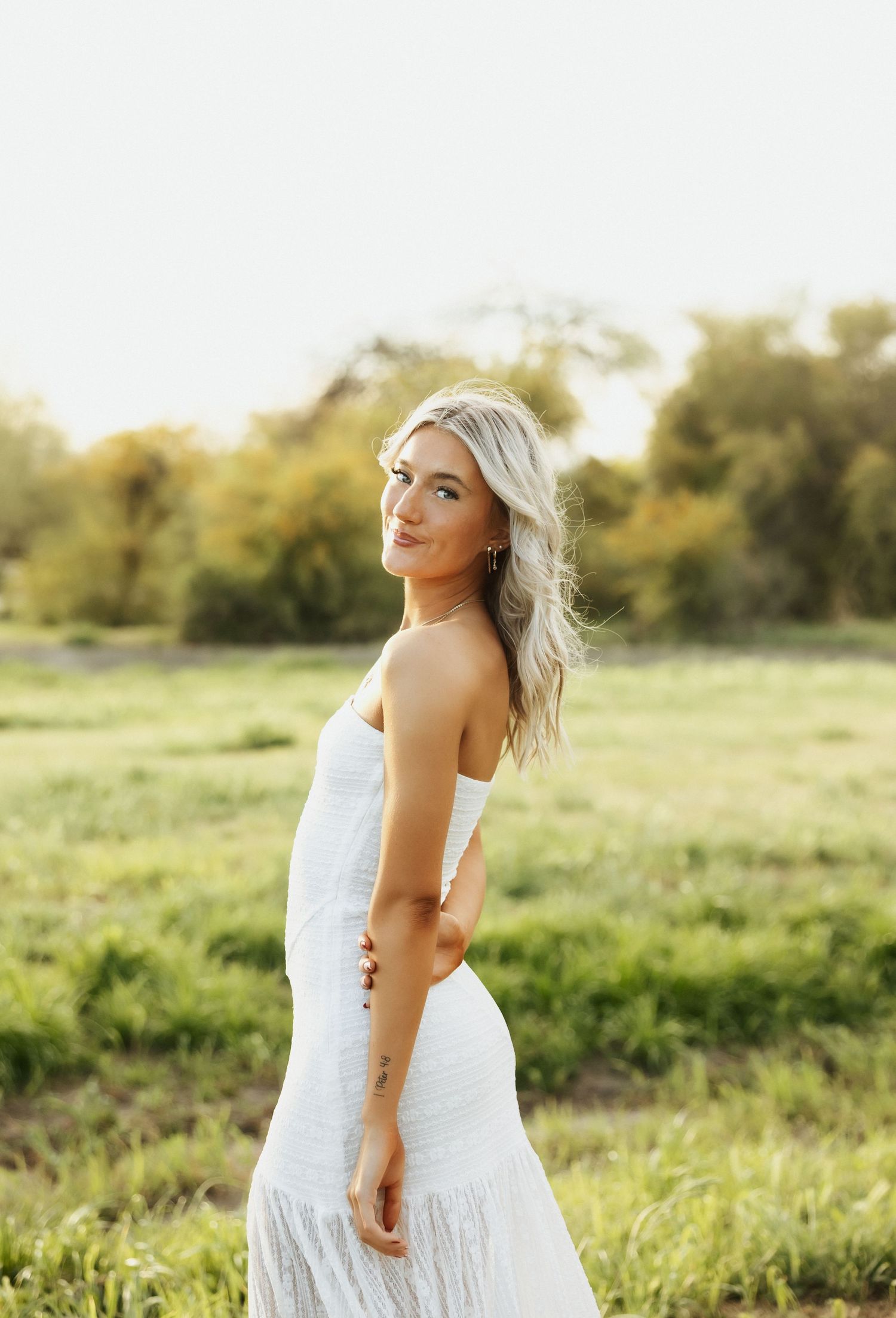 A person in a flowing white dress poses in a sunlit meadow during golden hour.