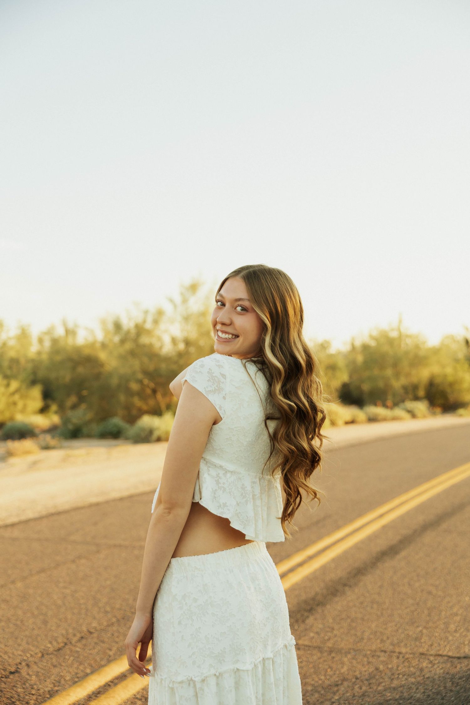 Arizona Desert Senior Photos Portraits on desert road at golden hour with warm sunlight creating dreamy atmosphere.