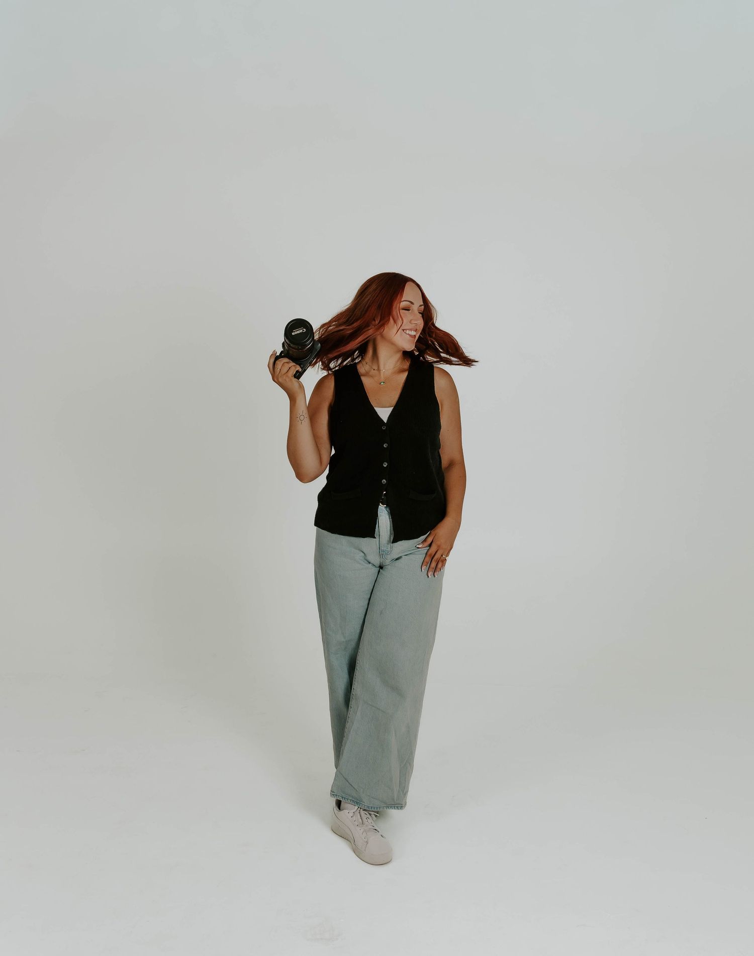 Fashion poses against light gray backdrop wearing black top and light denim.