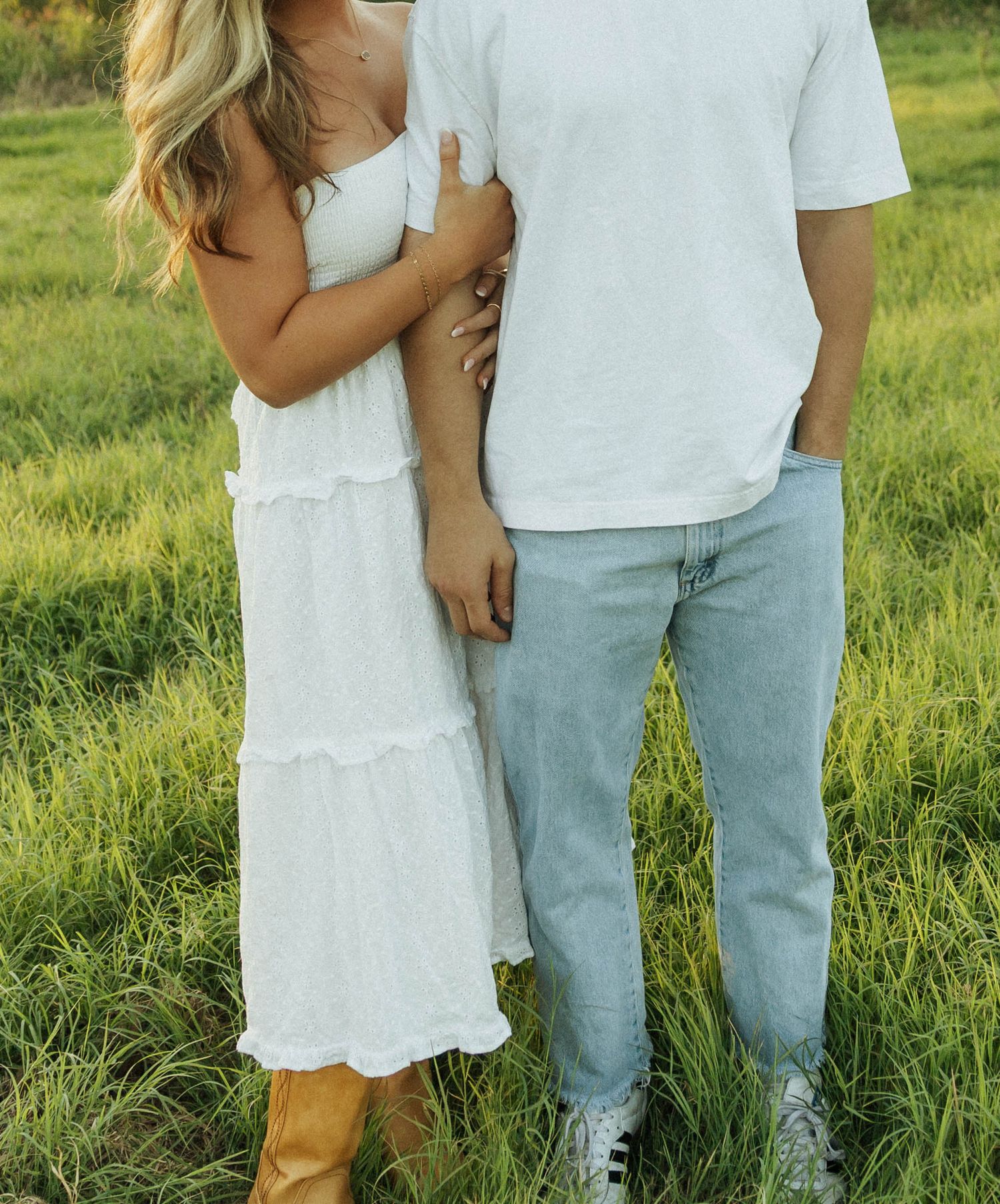 Couple in white outfits standing together in a grassy meadow during golden hour.