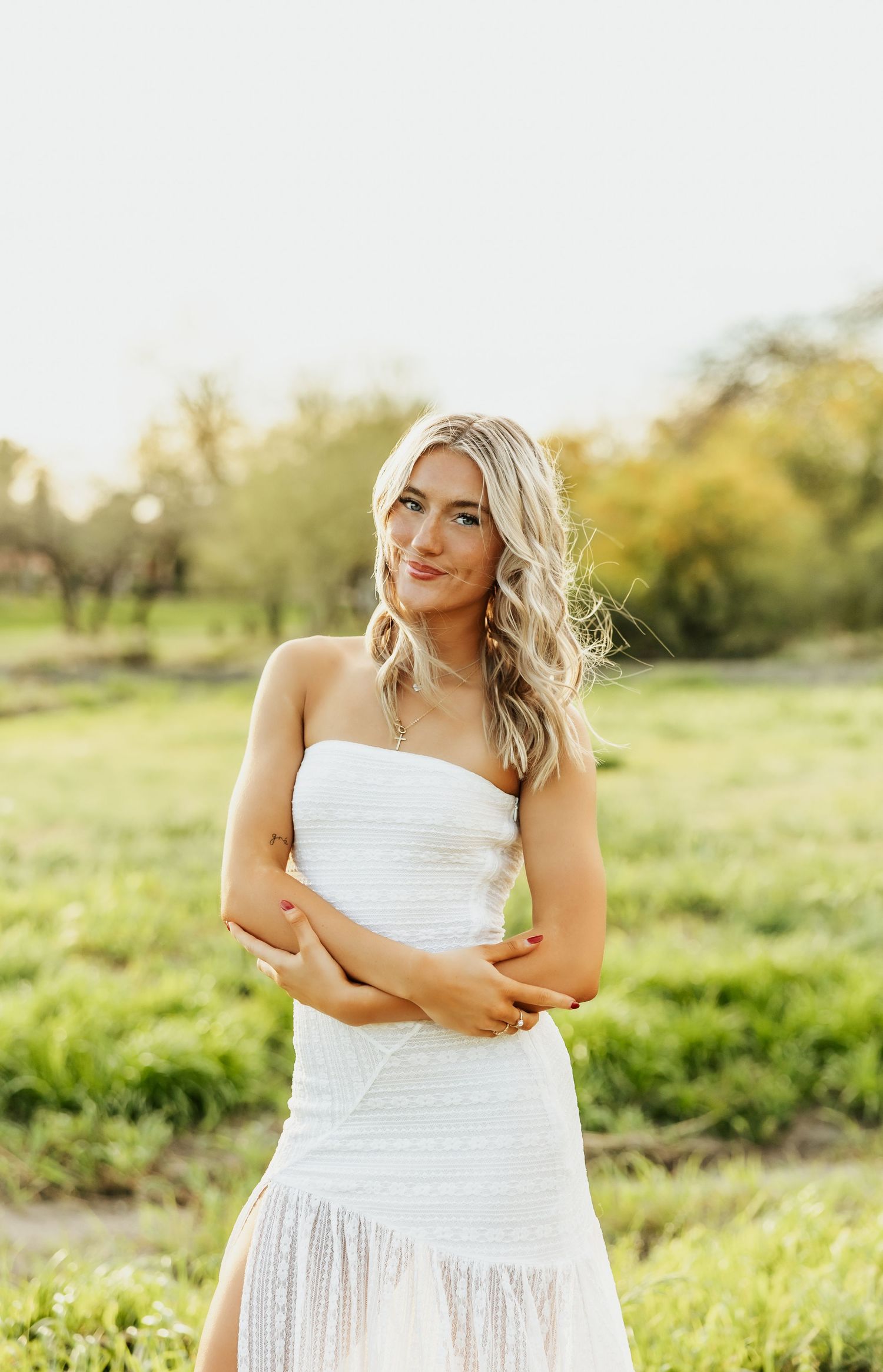 A woman in a flowing white dress poses gracefully in a sunlit meadow during golden hour.