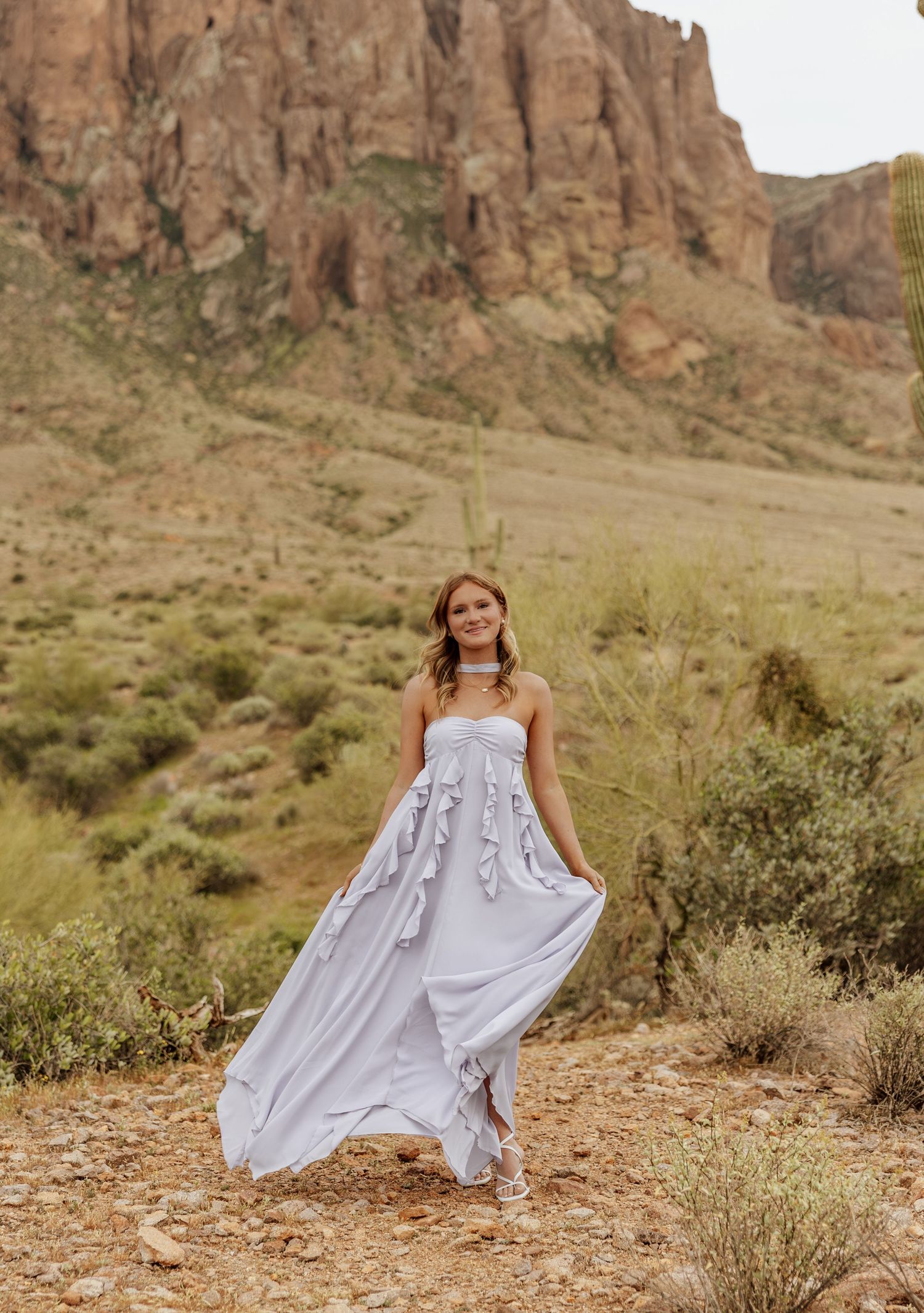 A flowing white dress twirls gracefully against the backdrop of rugged desert cliffs and desert brush in the afternoon light.