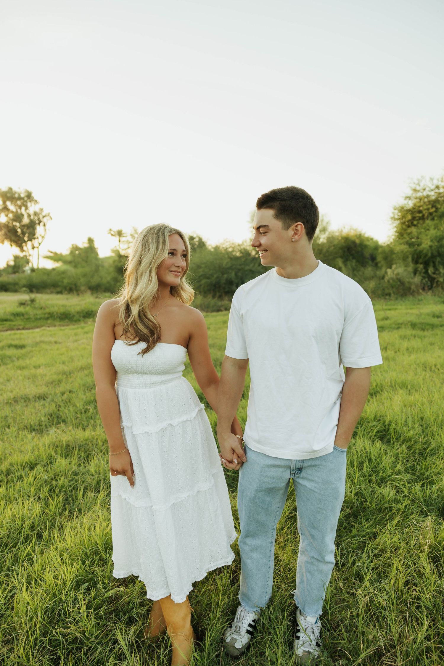 Playful couple walking through tall grass in matching white summer outfits.