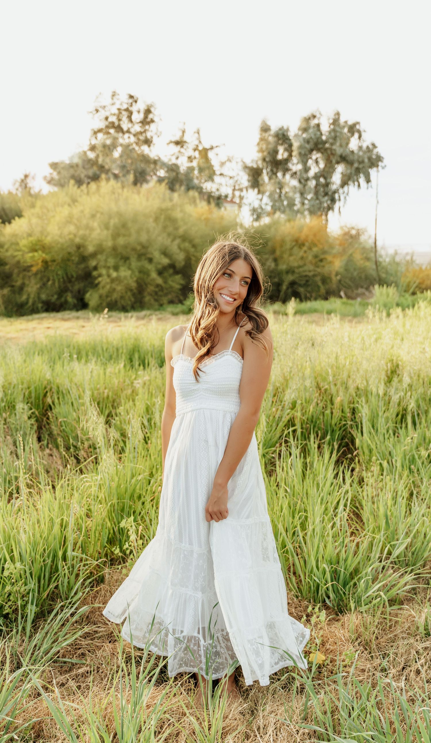 Two people in white dresses twirl and dance together in a sunlit meadow filled with tall grass and wildflowers.
