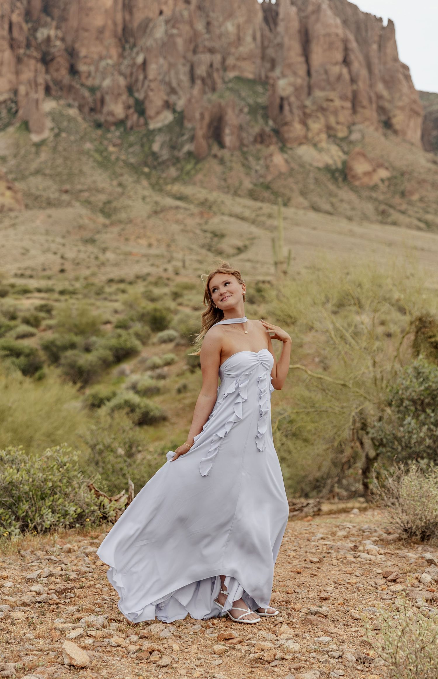 A flowing silver dress billows in the wind against a dramatic desert mountain backdrop.