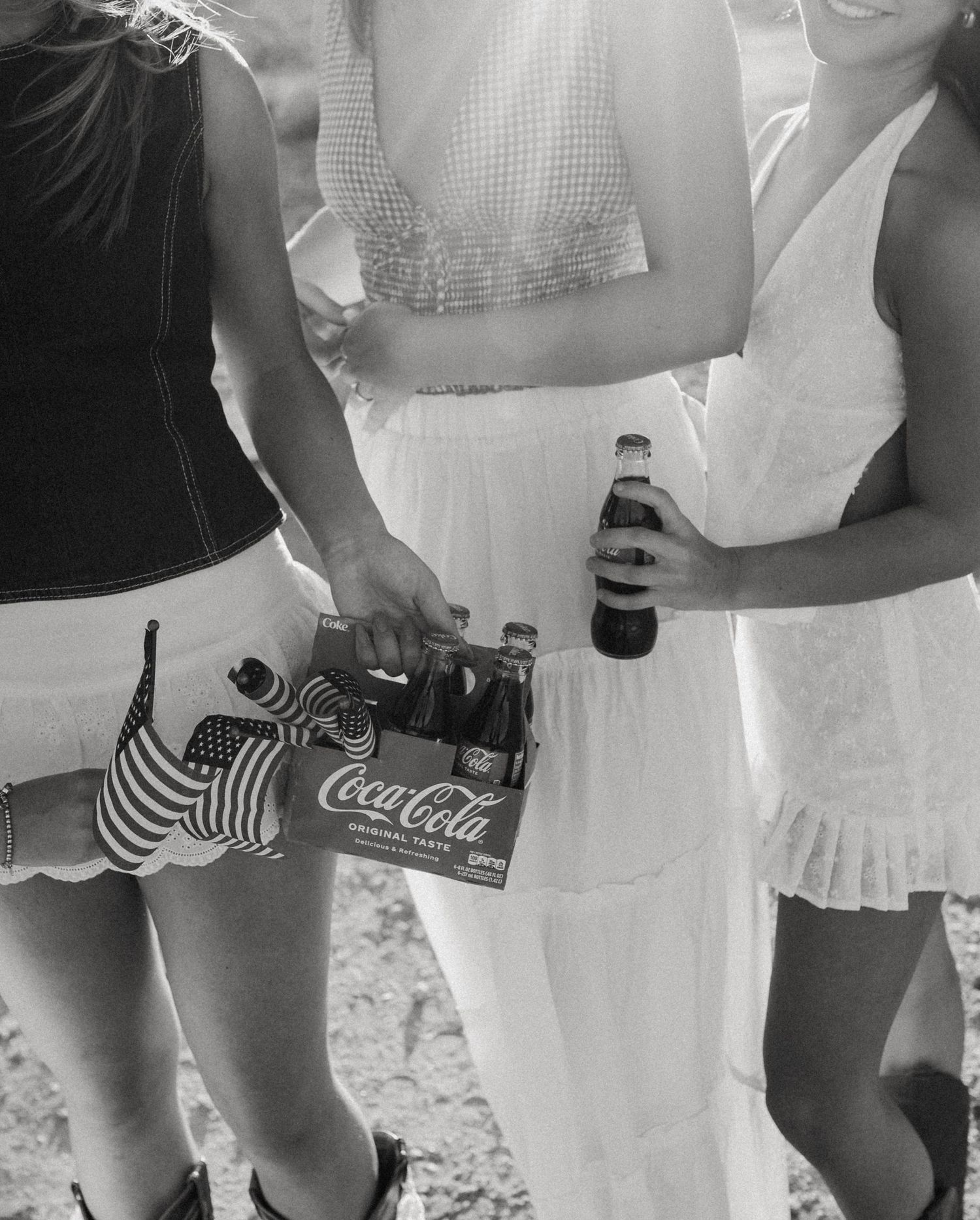 A vintage black and white photo showing people in summer attire holding Coca-Cola bottles.