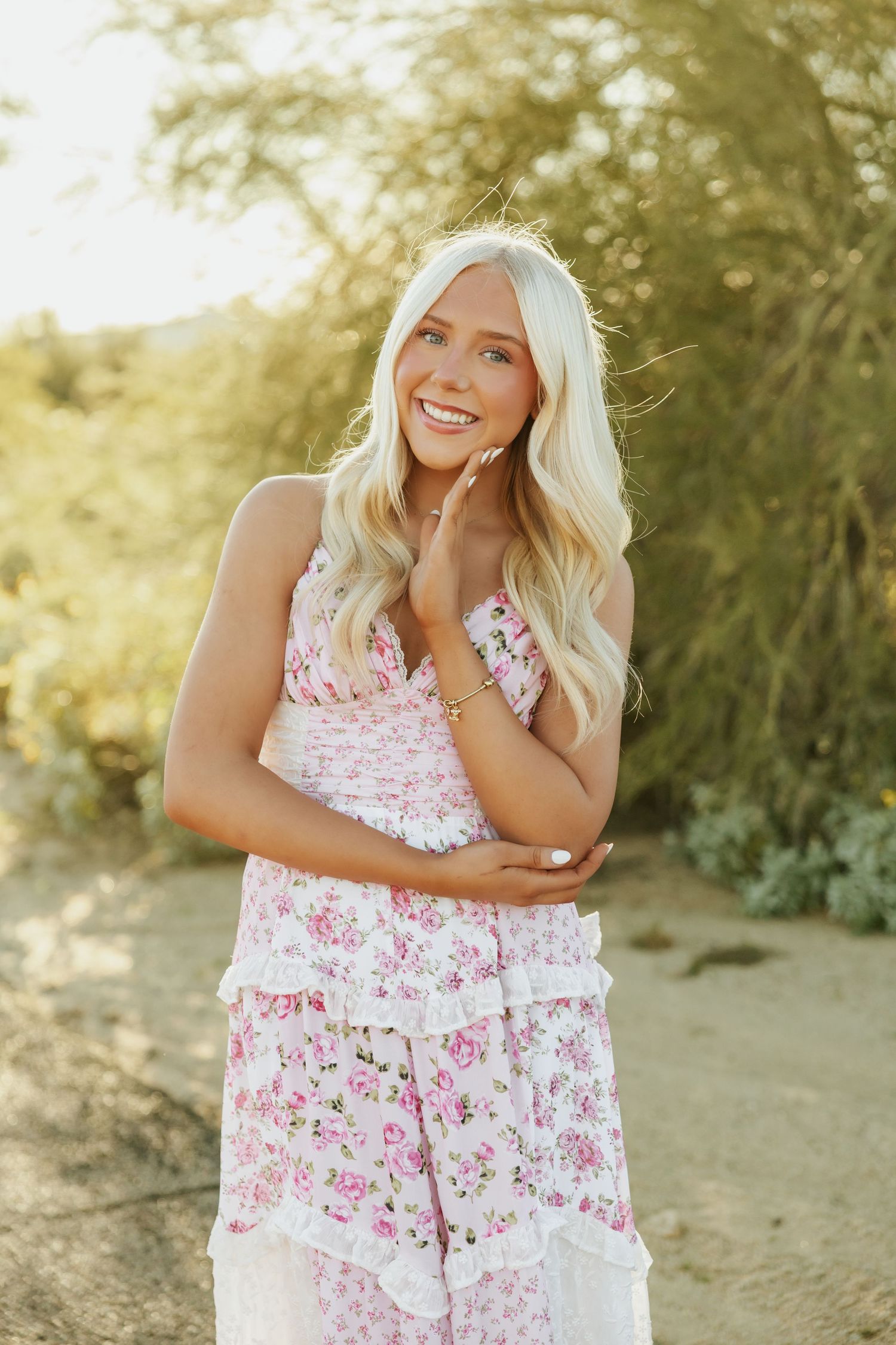 A woman in a pink floral dress poses outdoors in golden sunlight during a desert photoshoot.
