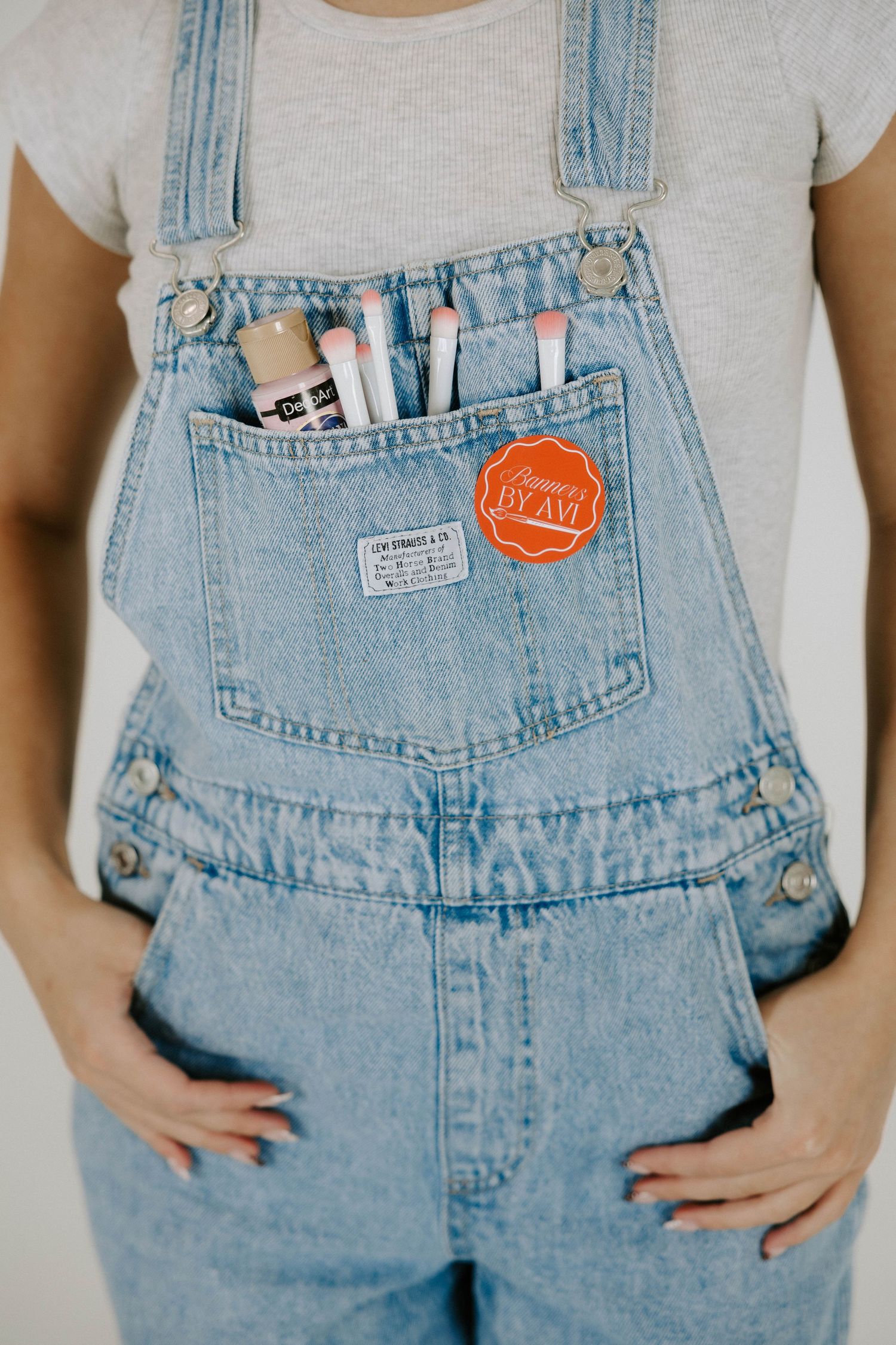 Light blue denim overalls with art supplies and a red circular sticker tucked into the front chest pocket.