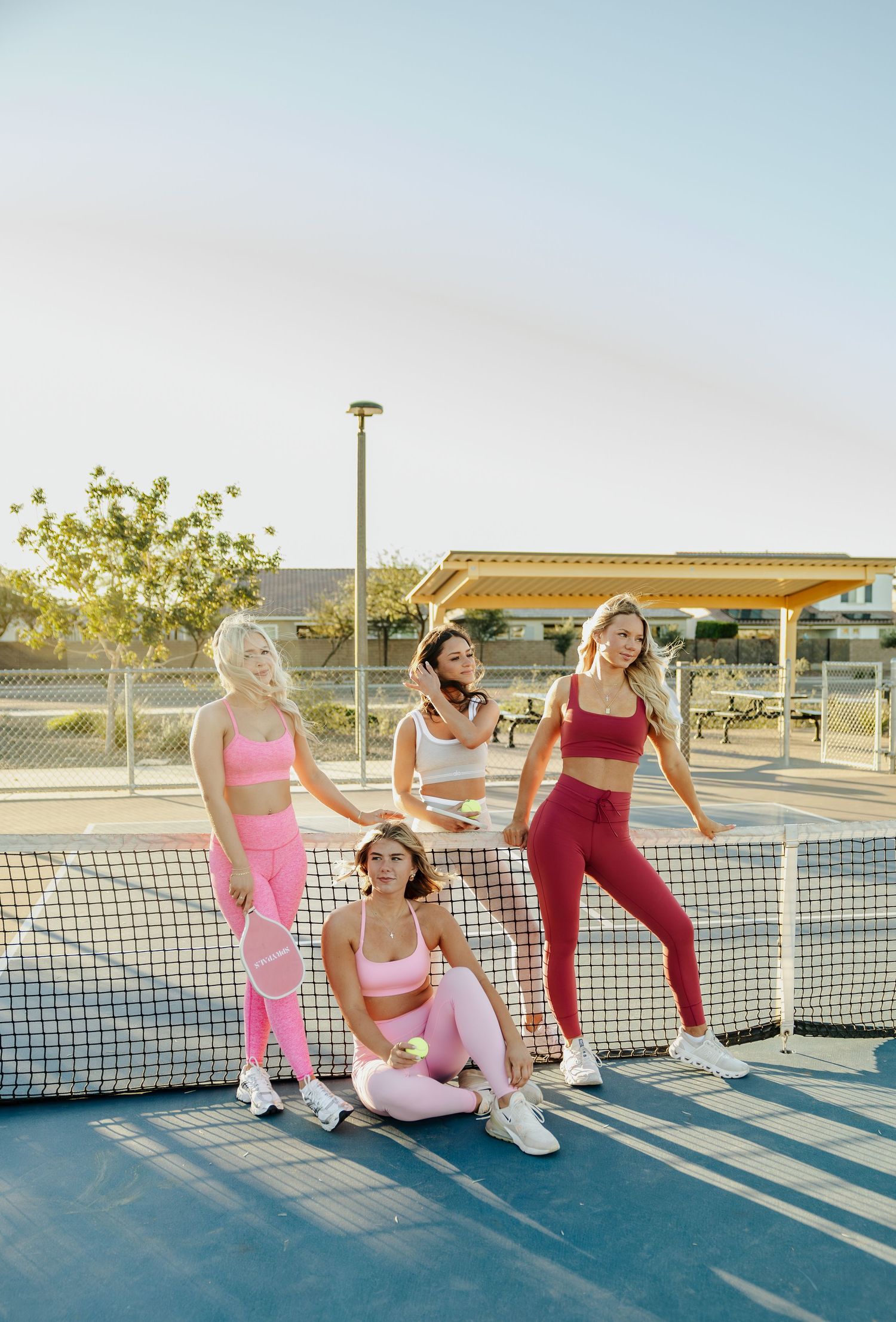 Athletes in athletic wear relax and stretch on a tennis court during sunset.