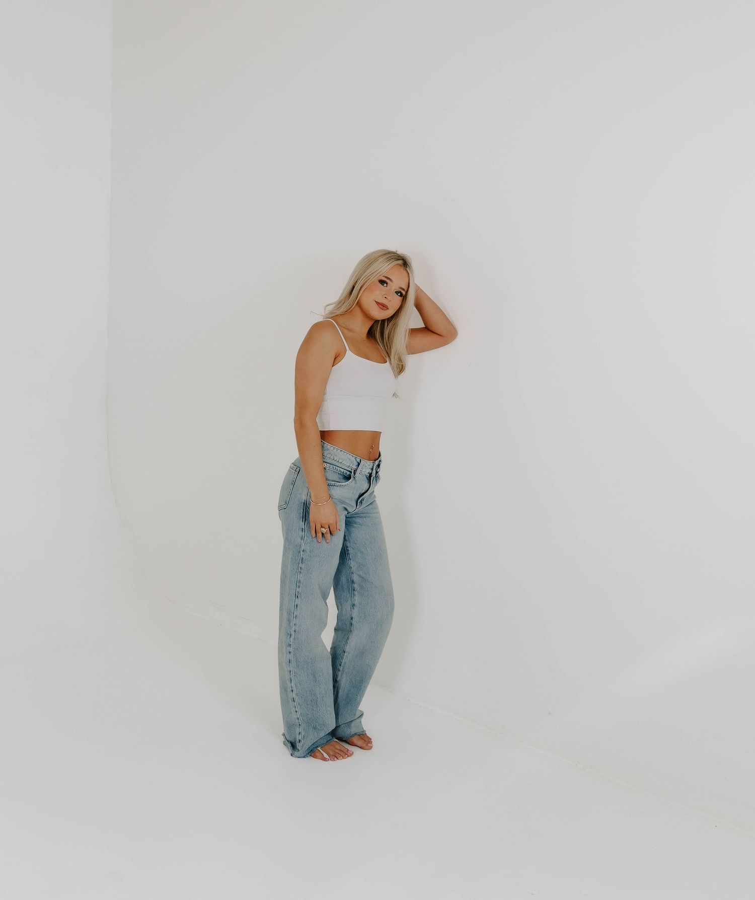 Modern fashion poses against white studio backdrop wearing denim and crop top.