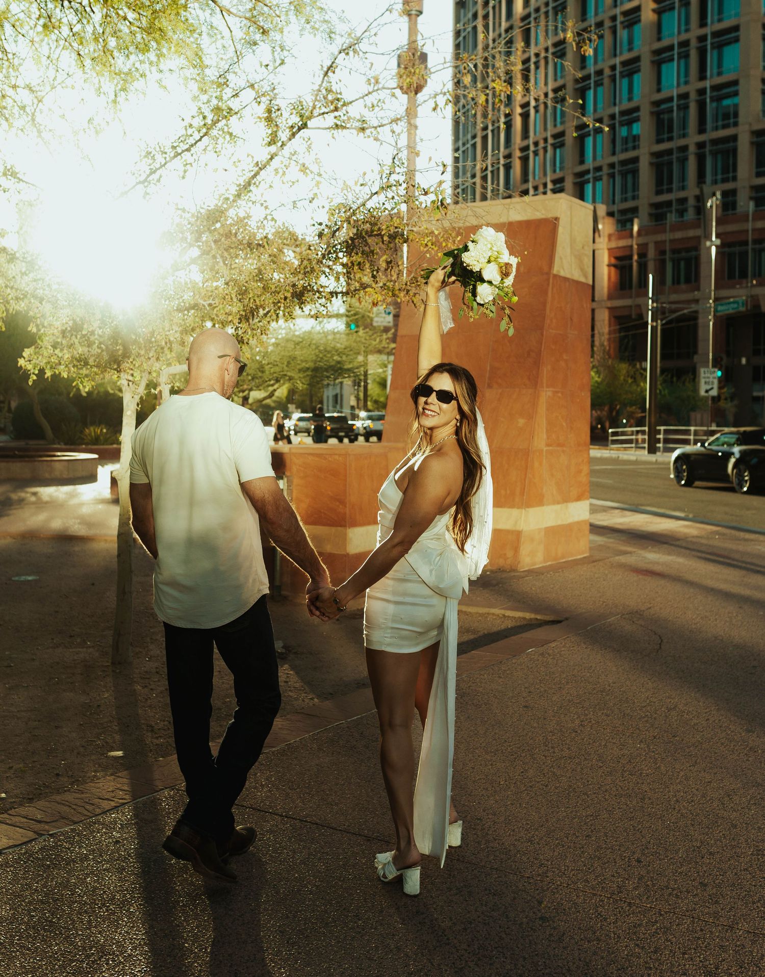 Couple walking together on a city sidewalk during sunset with golden sunlight creating a romantic atmosphere. Elopement Photographer