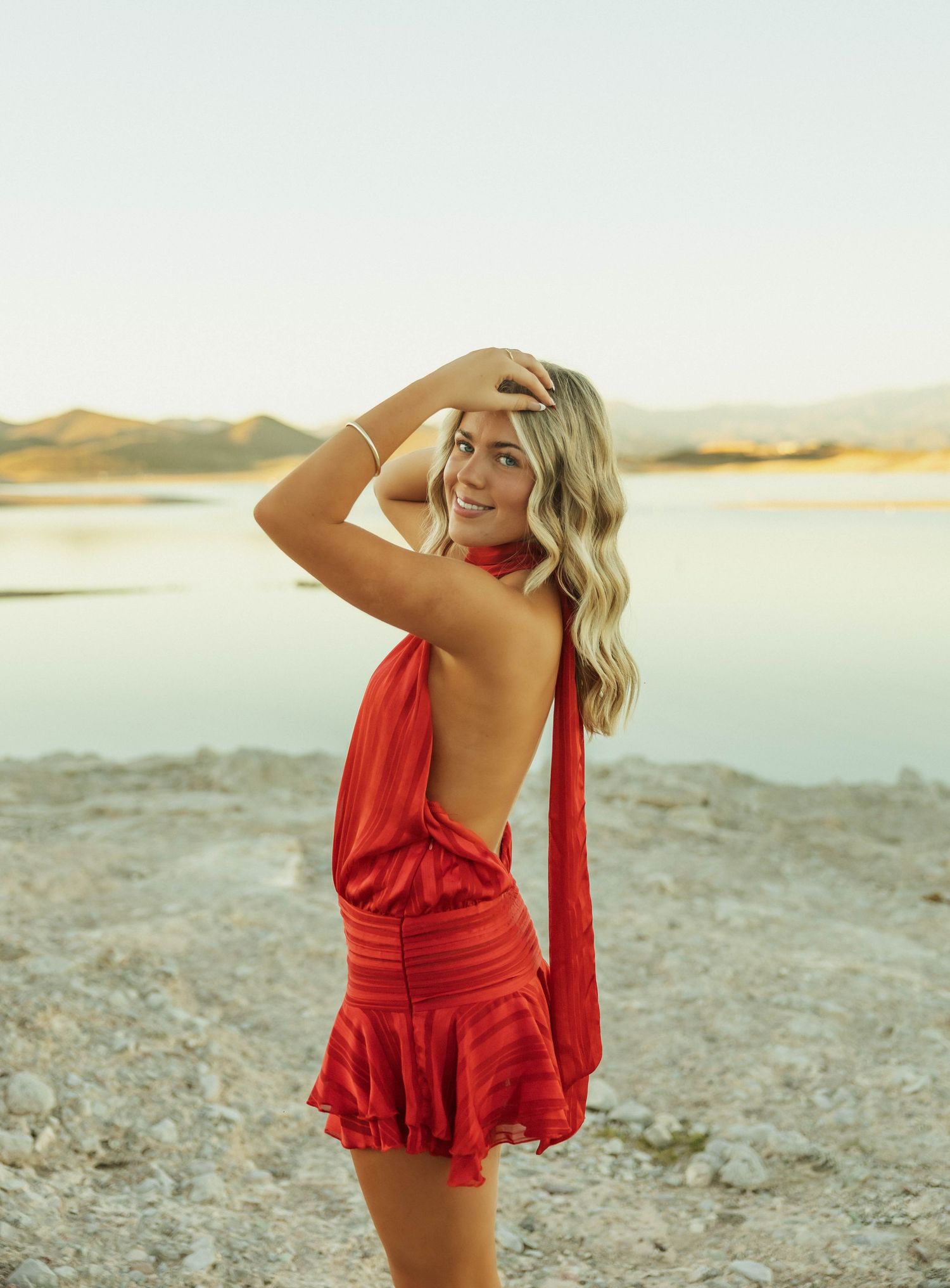 Woman in red ruffled dress poses playfully against desert landscape at sunset.