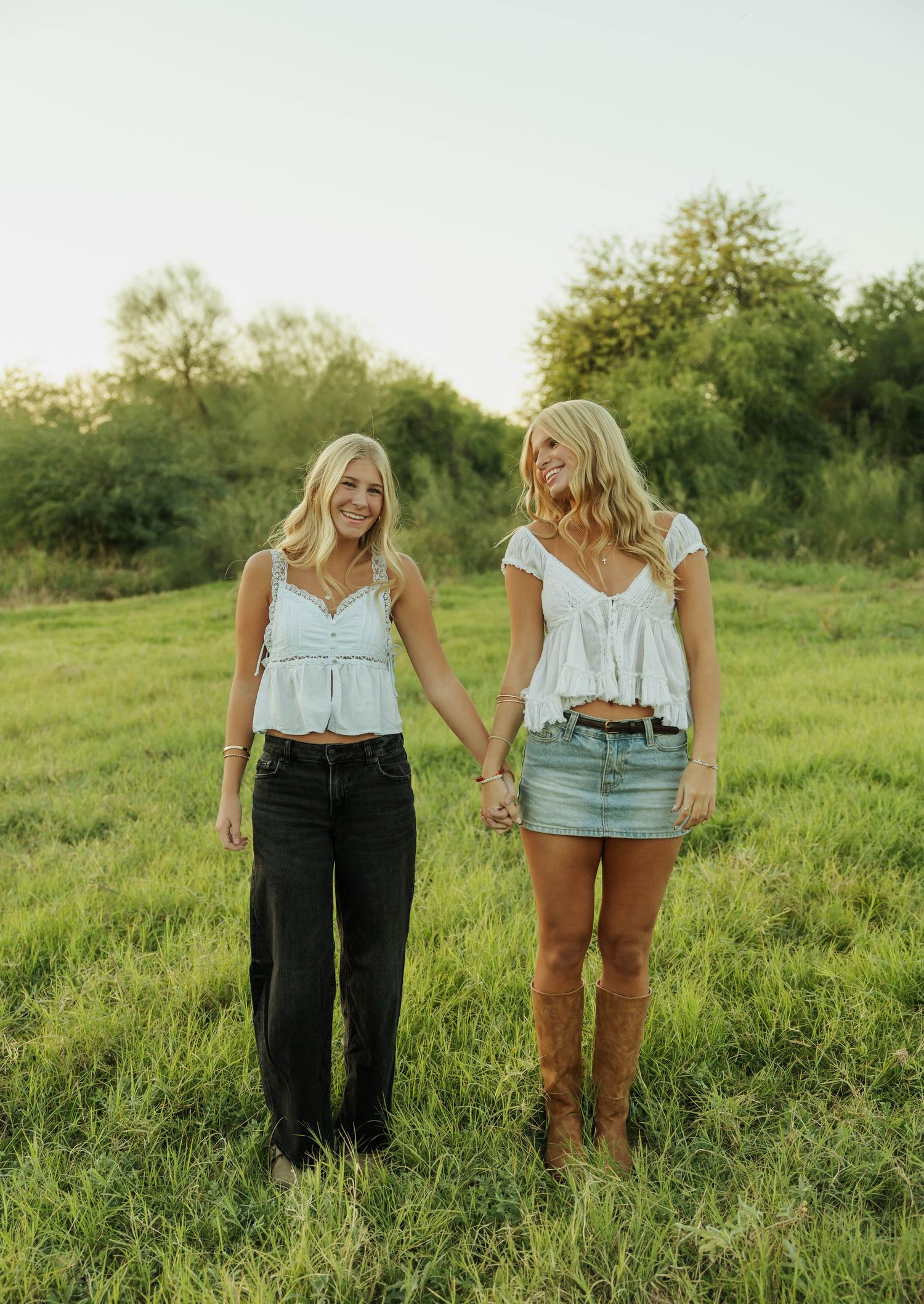 Two people wearing white tops stand together in a sunlit grassy field on a summer evening.