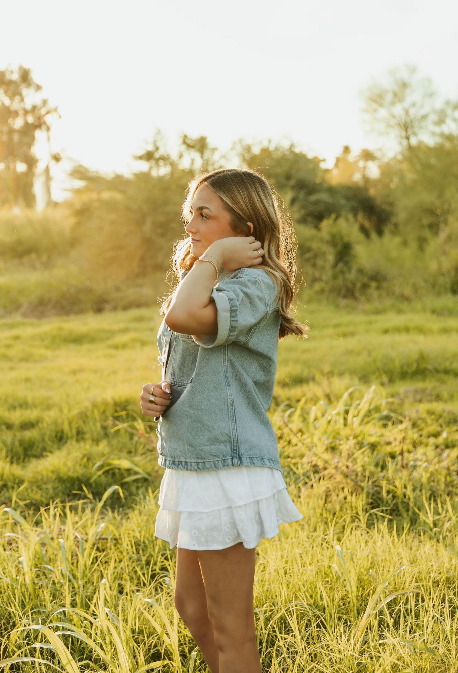 Woman in denim jacket standing thoughtfully in golden evening light.