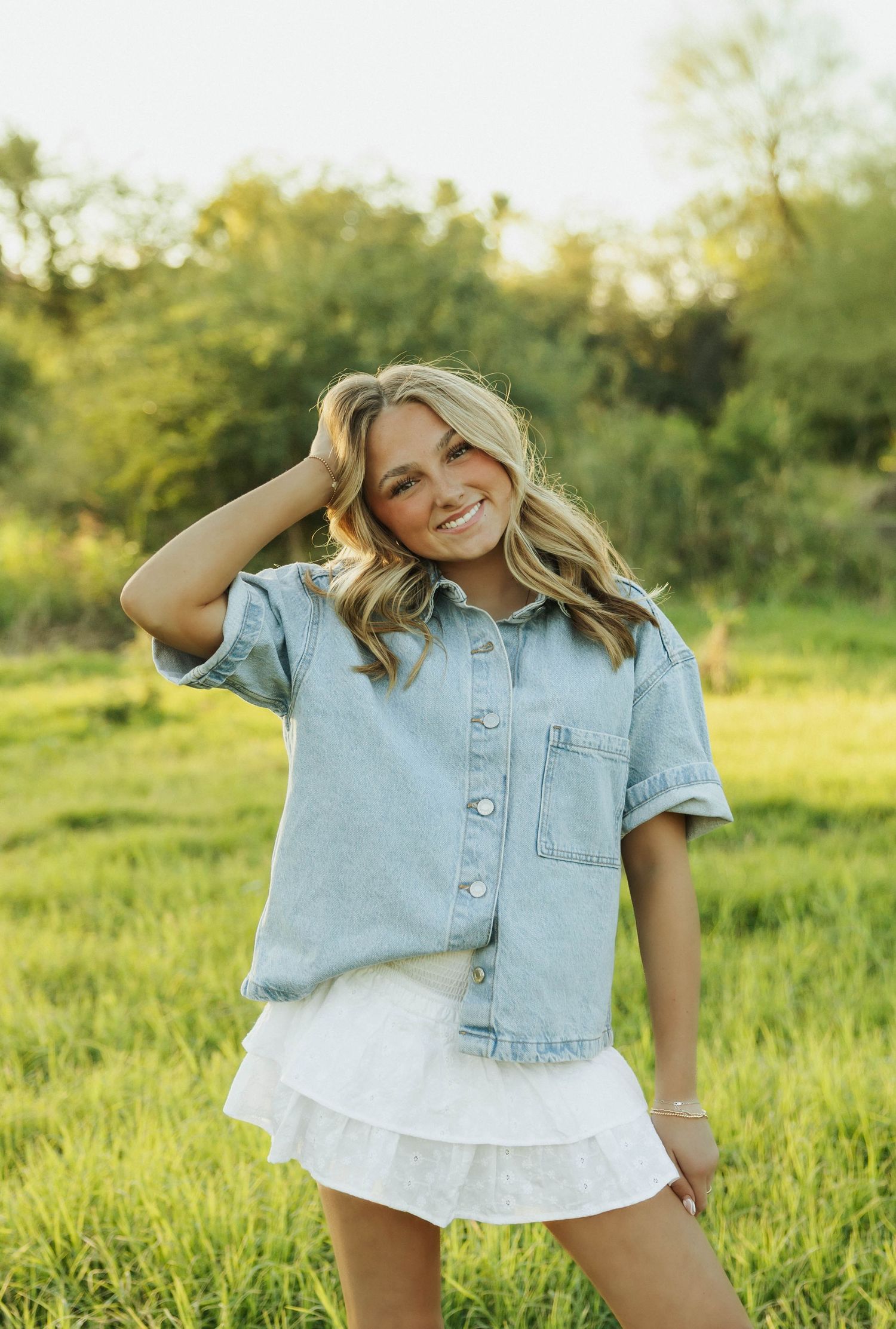 Candid moments in light denim jacket against green summer landscape. Senior photos