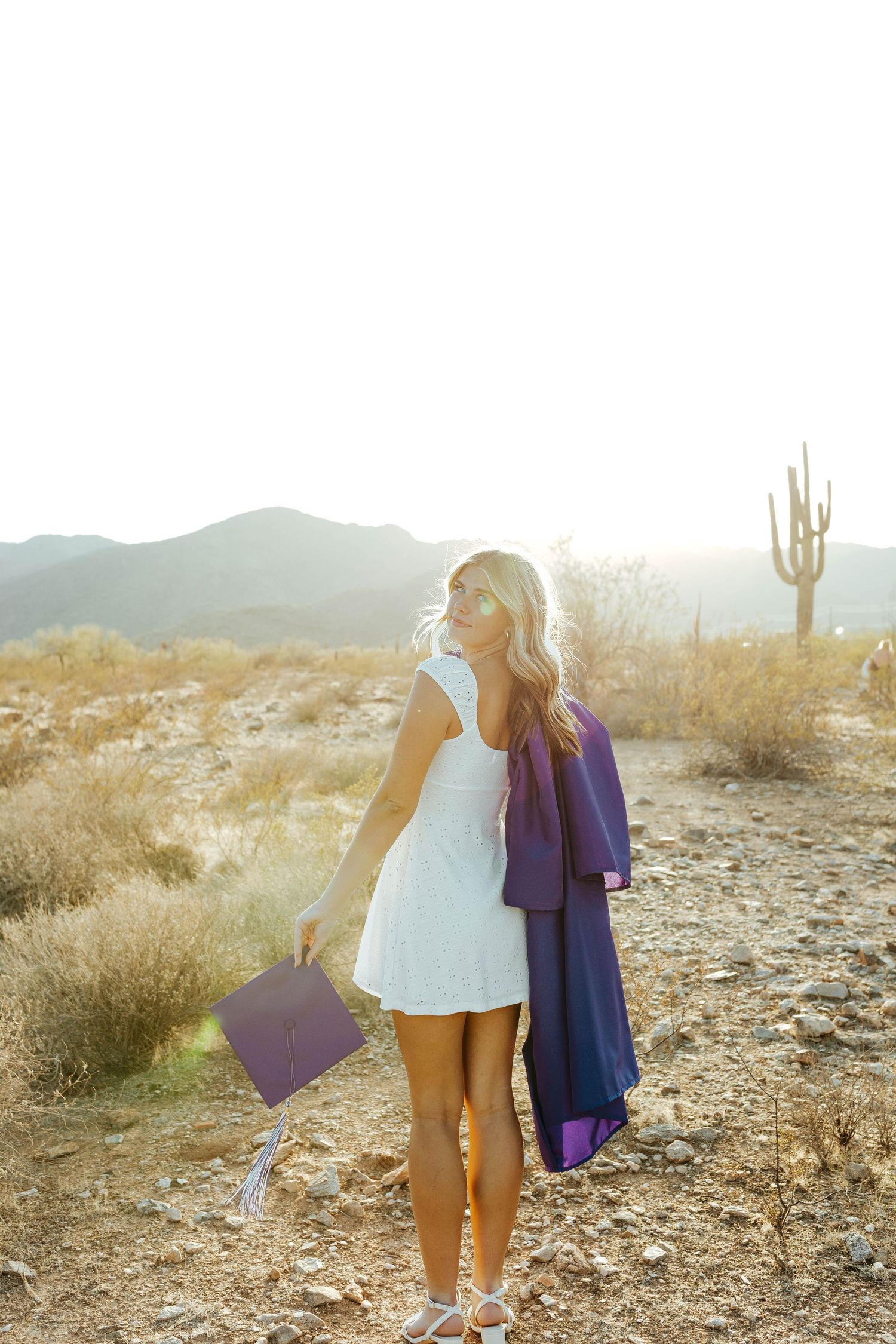 Purple graduation gowns being held up in a desert setting with saguaro cacti.
