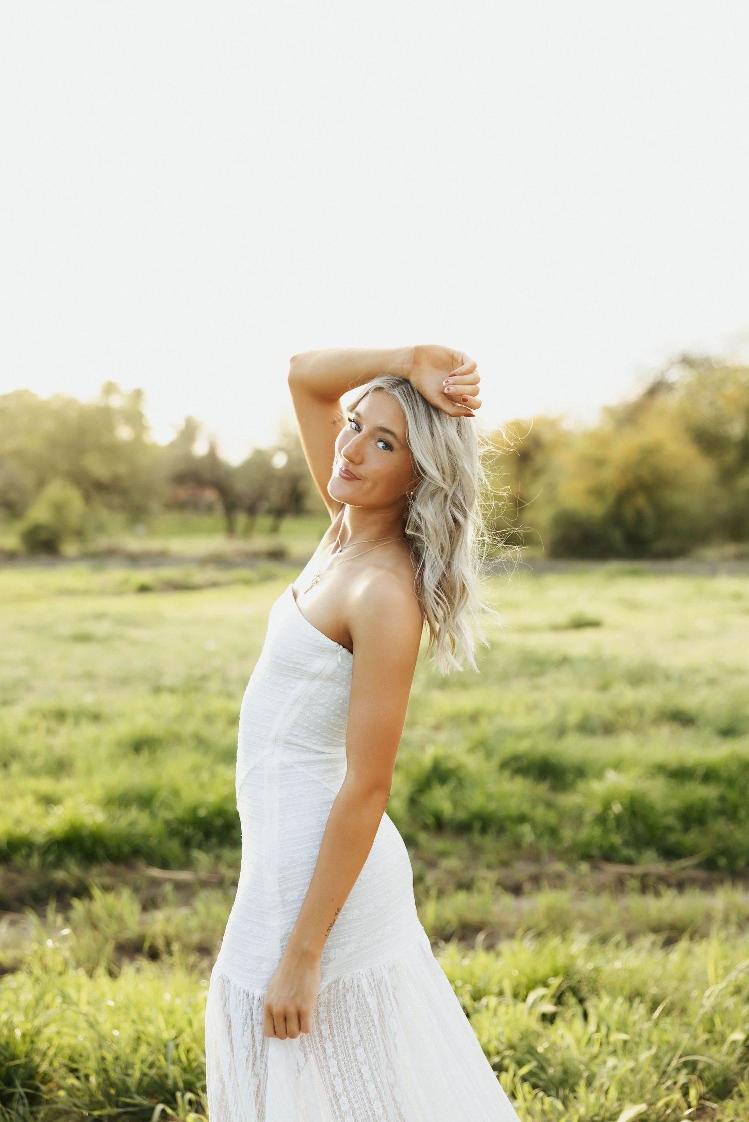 Woman in flowing white dress twirls joyfully in a sunlit meadow during golden hour.