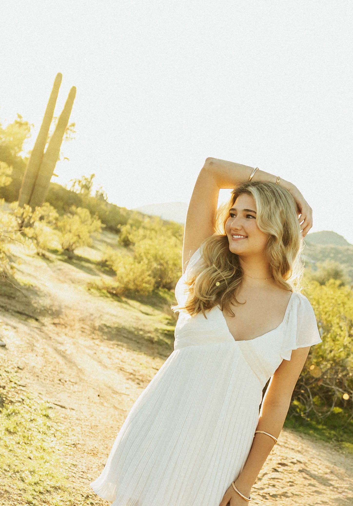 Golden hour desert senior portraits with white dress and cactus silhouettes.