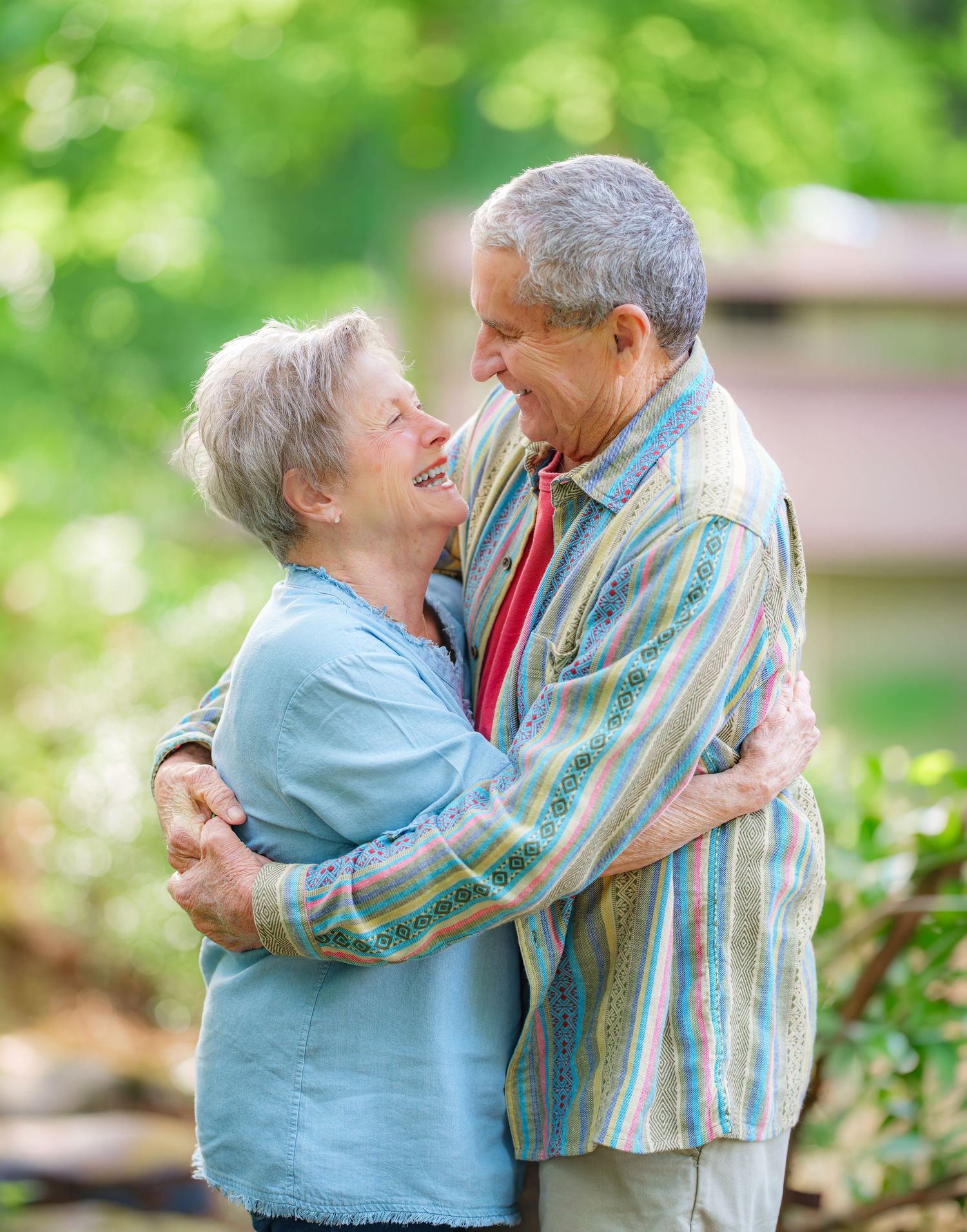 Happy senior couple embracing and smiling at each other outdoors in a lush green garden setting.