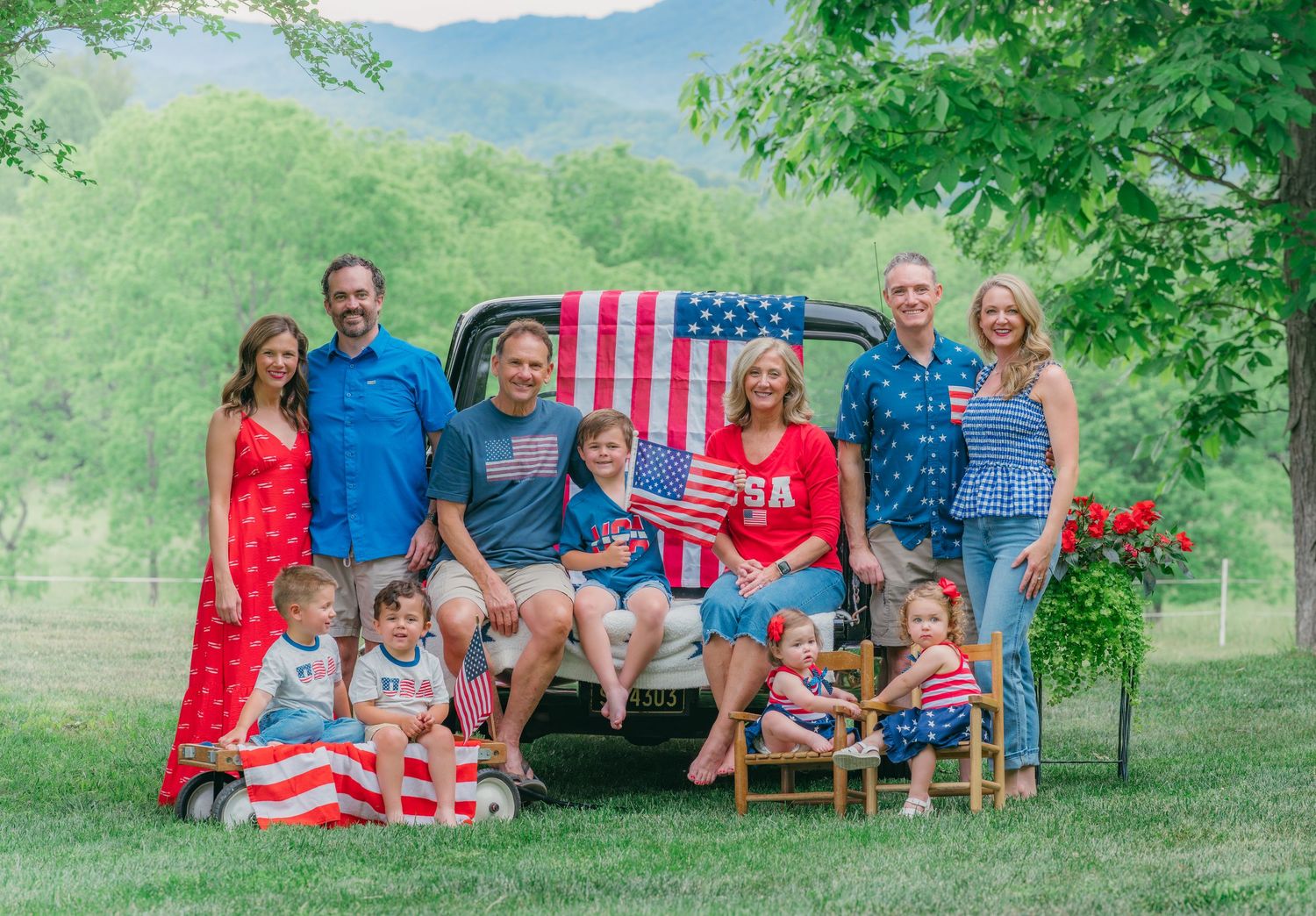 Large family group posing patriotically with American flags by a vintage truck outdoors.