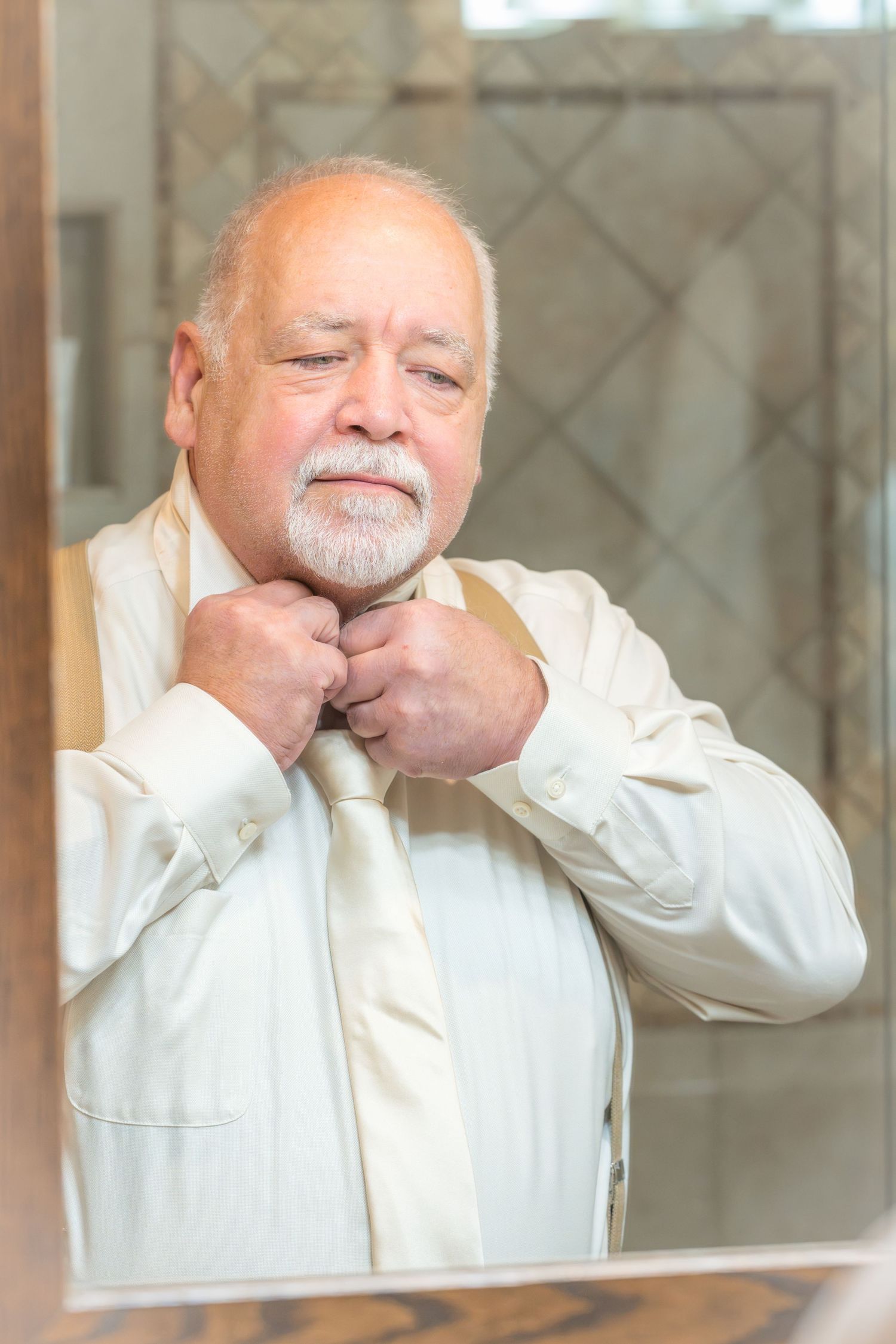 Senior man adjusting his tie in the mirror while getting dressed in a white shirt at the Roosevelt Lodge.