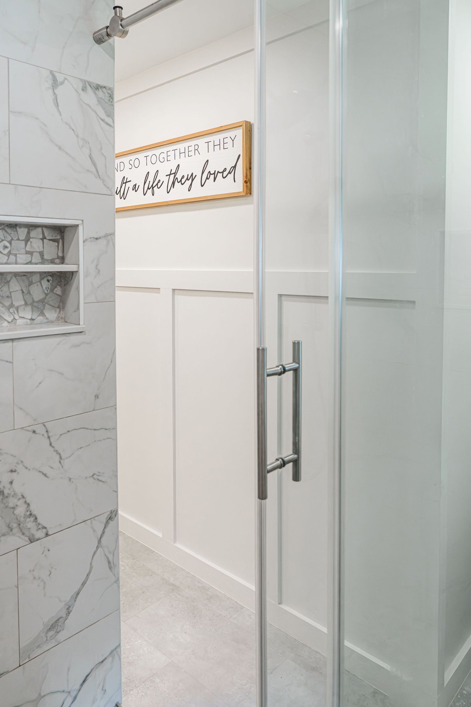 Modern bathroom with marble tile shower, frosted glass door, built-in niche, and decorative white board and batten wall.