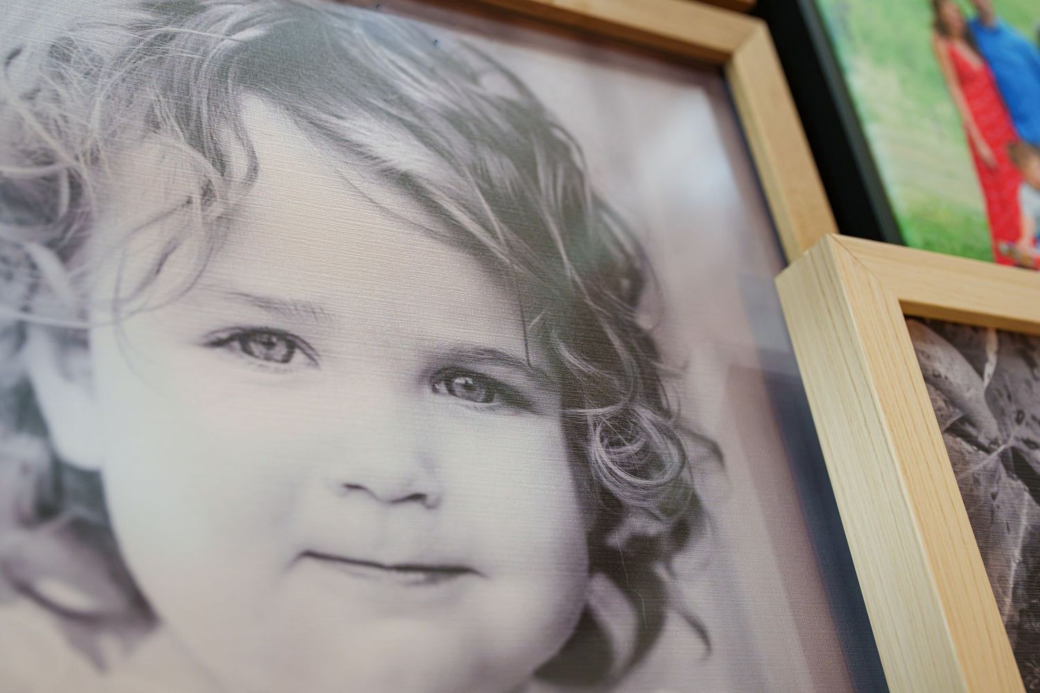 Black and white framed portrait photo of a cute curly-haired toddler girl smiling, displayed alongside colorful framed pictures.