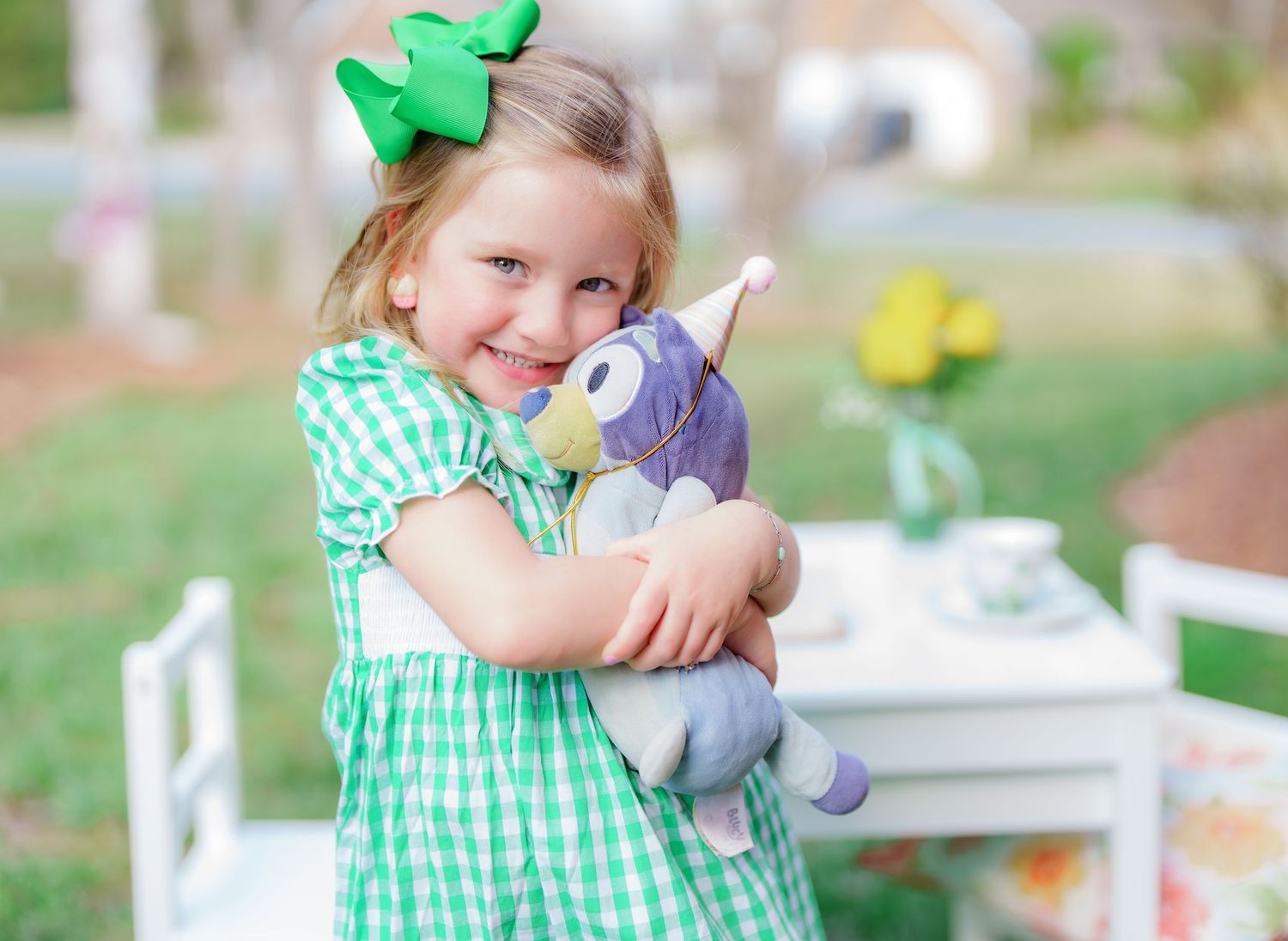 Young girl in green gingham dress hugging a stuffed animal toy, wearing a green bow in her hair.