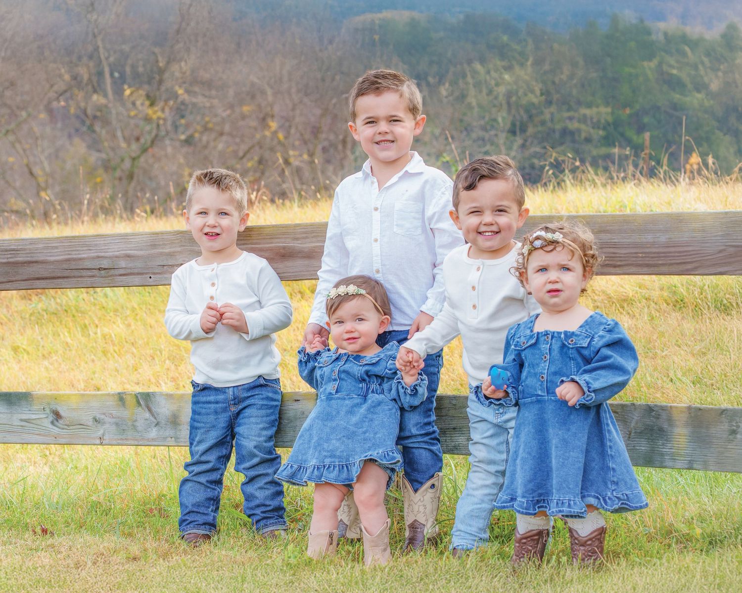 Five young children posing together by a wooden fence in coordinating blue and white outfits.
