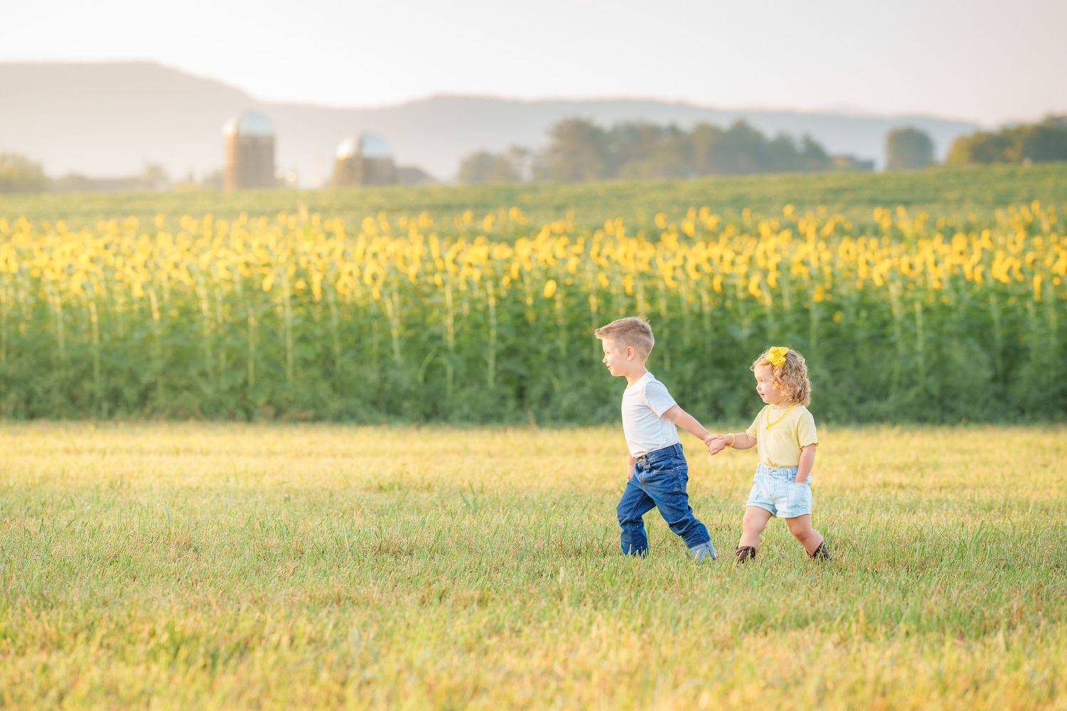 Two young children holding hands and running through a sunflower field on a sunny day.