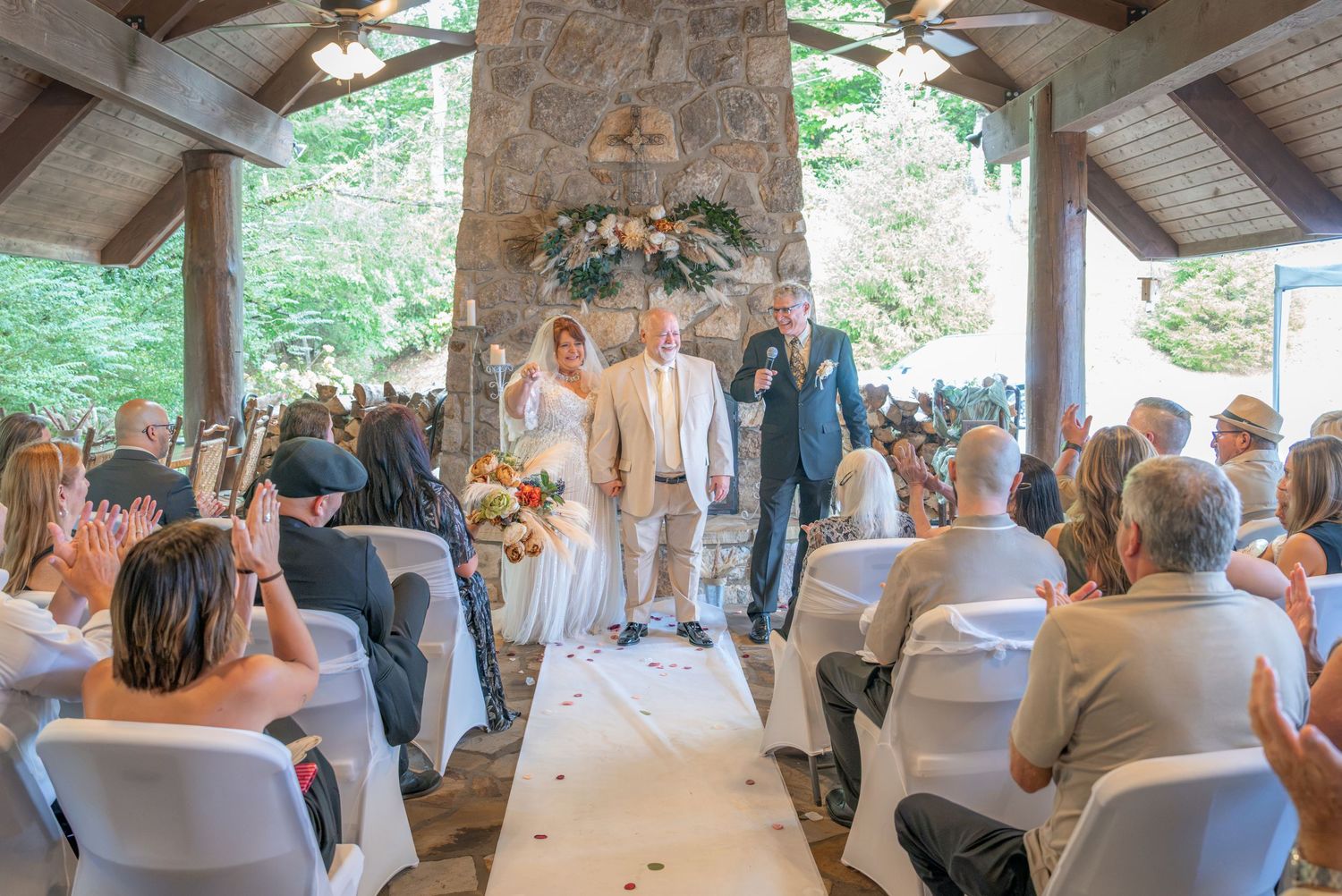 Couple exchanges vows at elegant outdoor wedding ceremony in rustic stone pavilion surrounded by applauding guests.