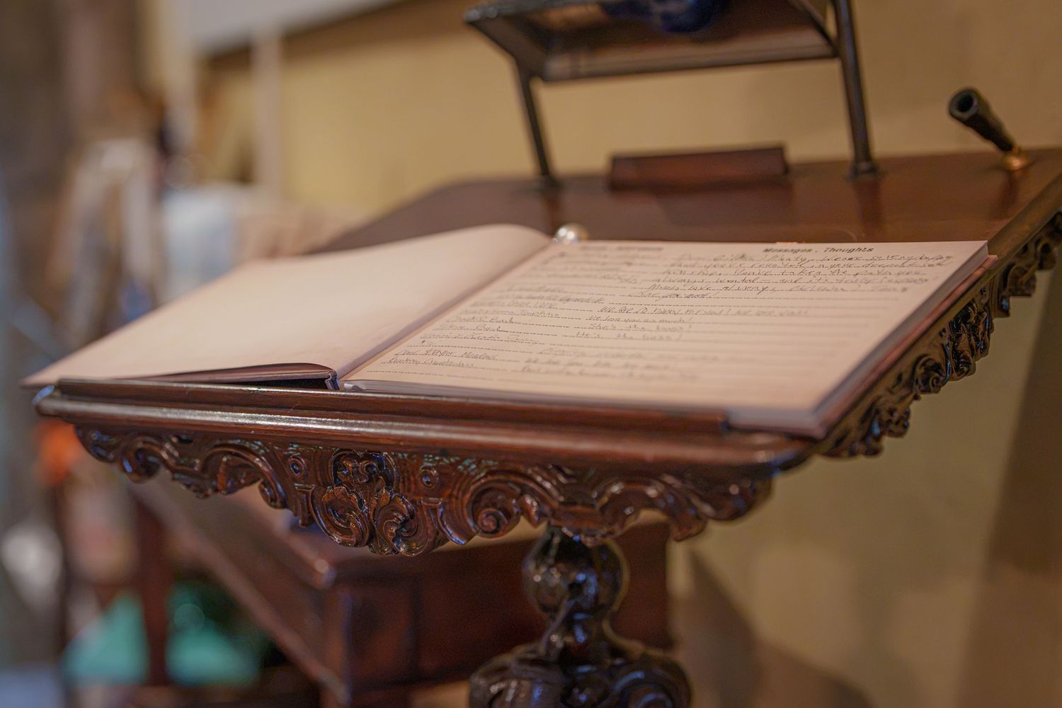 Ornate carved wooden book stand displaying an open handwritten manuscript in an antique setting.