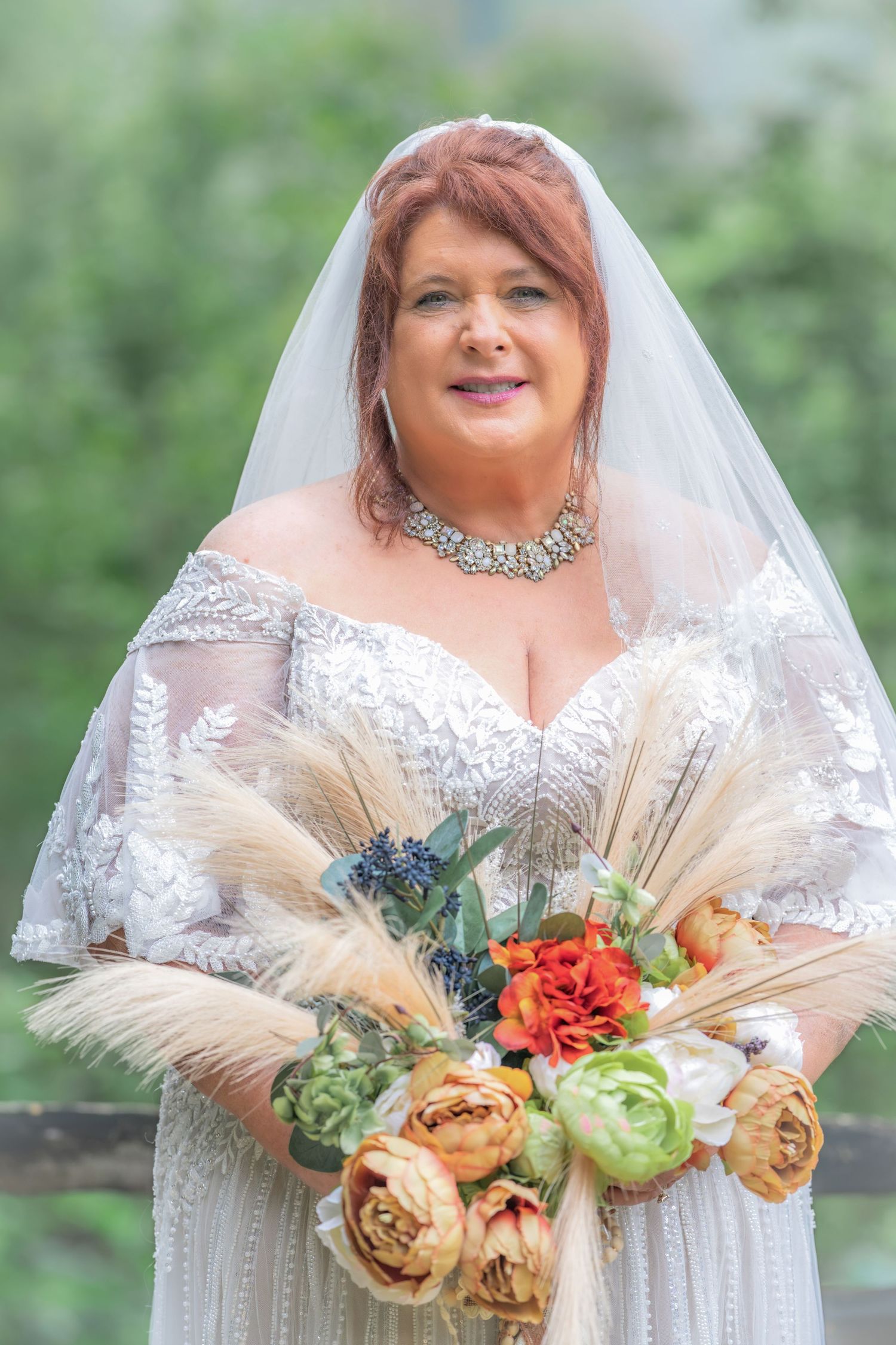 Bride in lace off-shoulder gown and veil holds boho bouquet with pampas grass and roses in Gatlinburg, TN.