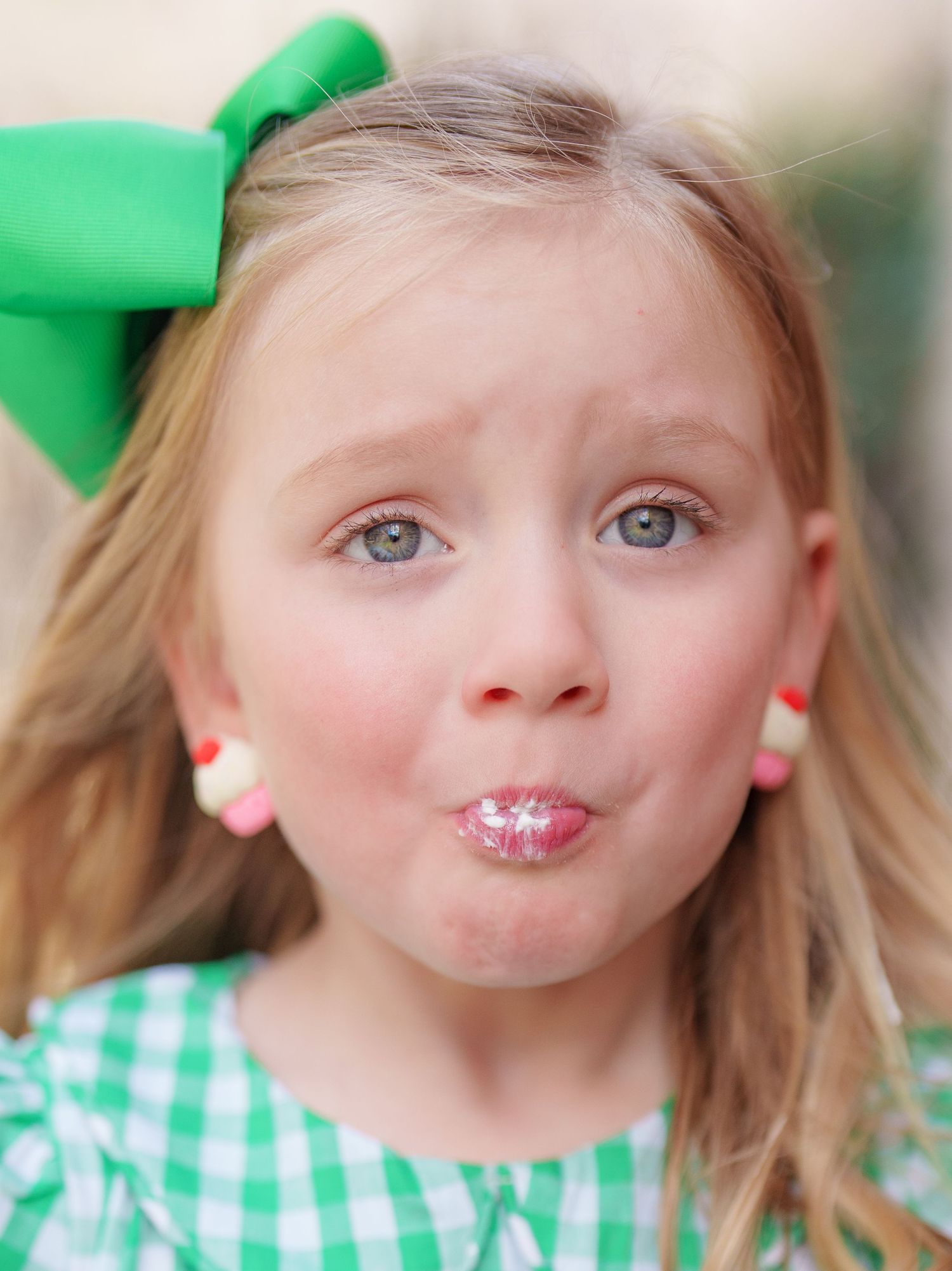 Close-up of a cute young girl with a green bow making a funny pouty face with glittery pink lips.