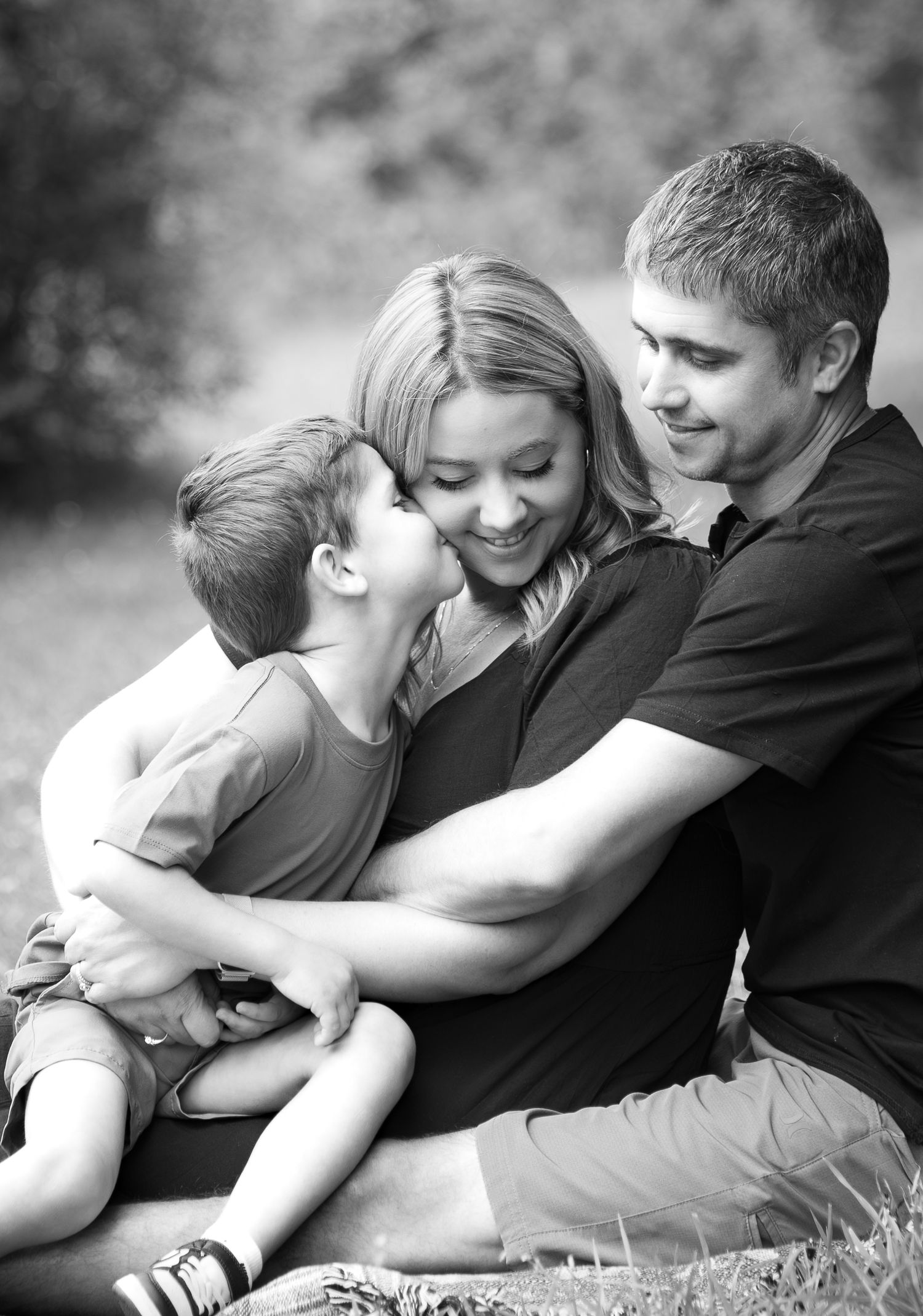 Black and white family portrait of parents and young son sharing a tender moment outdoors.