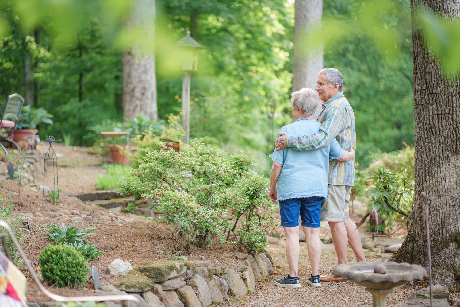 Elderly couple with arms around each other admiring a lush garden landscape together.