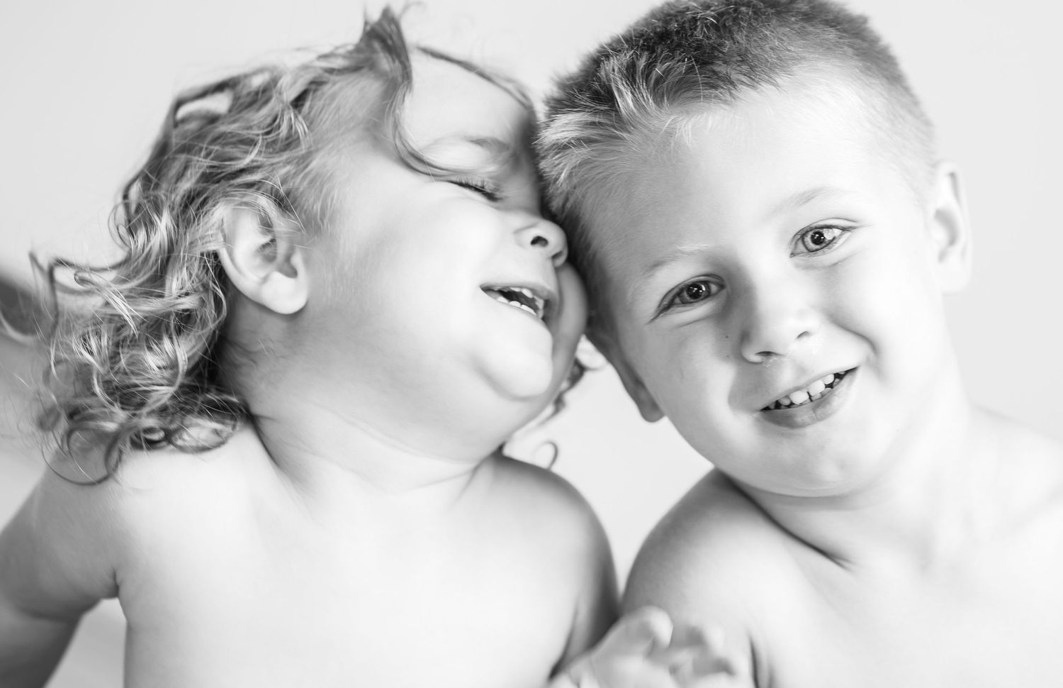 Black and white photo of two happy young children laughing and smiling together in a joyful candid portrait.