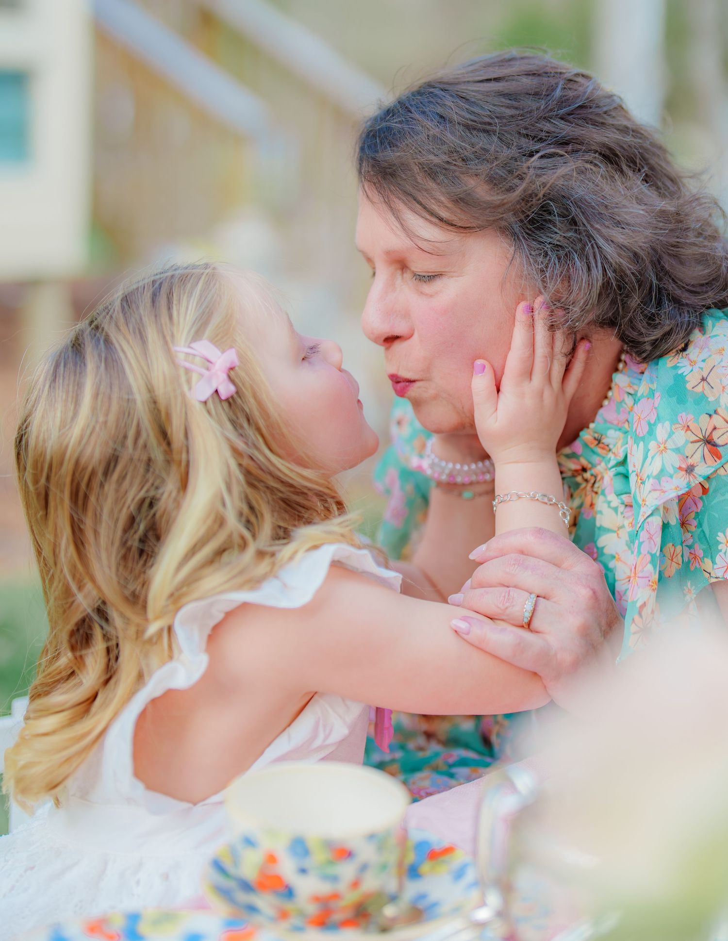 A young blonde girl tenderly holds an older womans face for a sweet kiss.