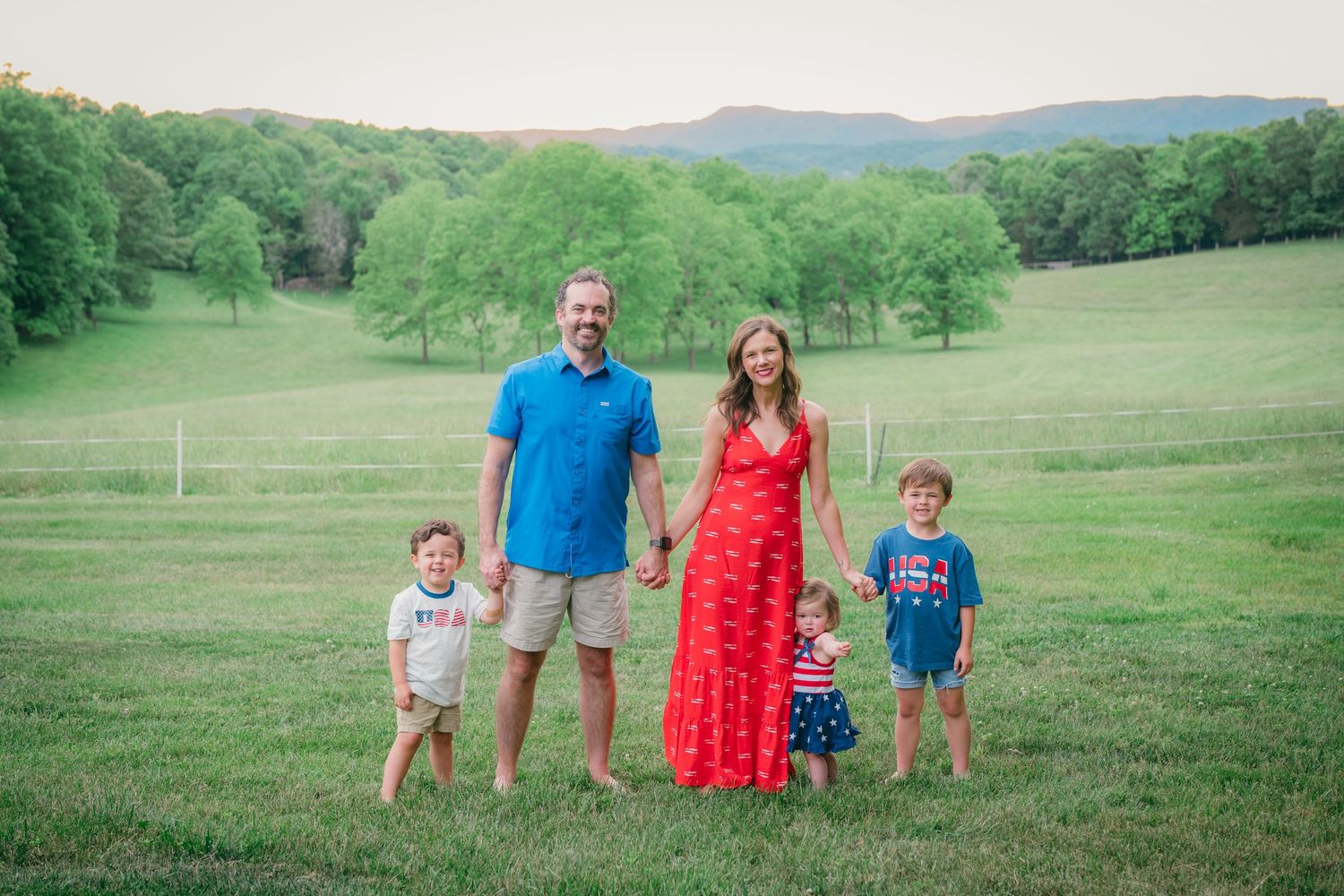 Family of five poses in a green meadow with rolling hills wearing red, white, and blue.