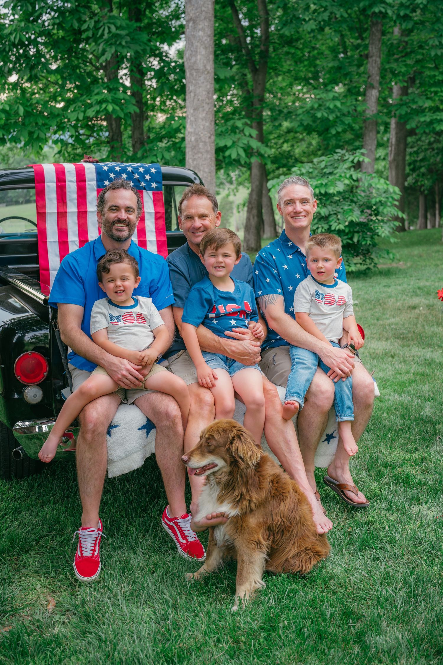Family with three kids and a dog pose on vintage truck tailgate with American flag for Fourth of July photo.