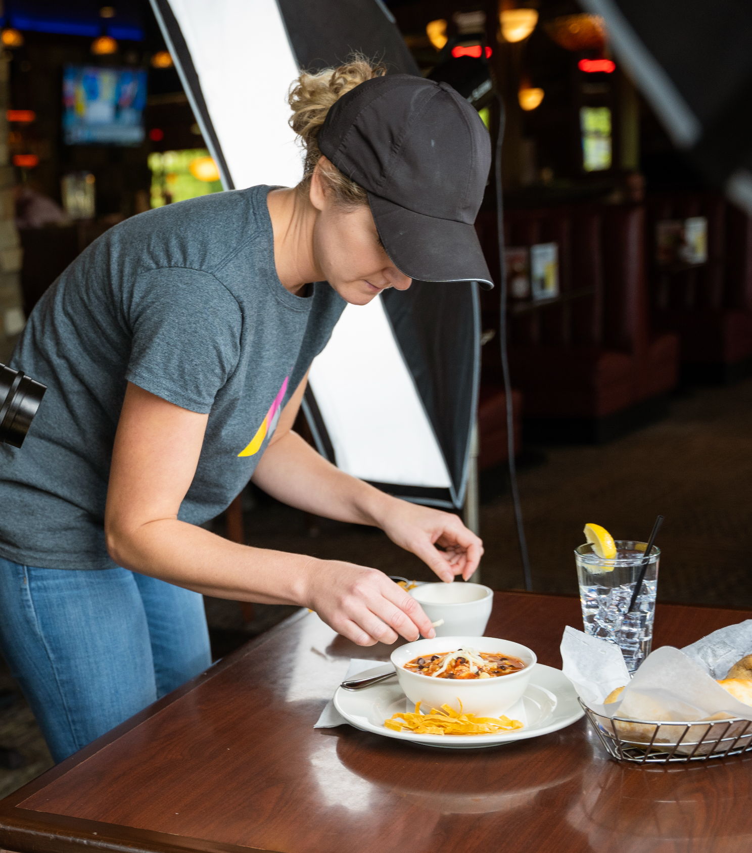 Female food photographer styling a bowl of chili under studio lights in a restaurant.