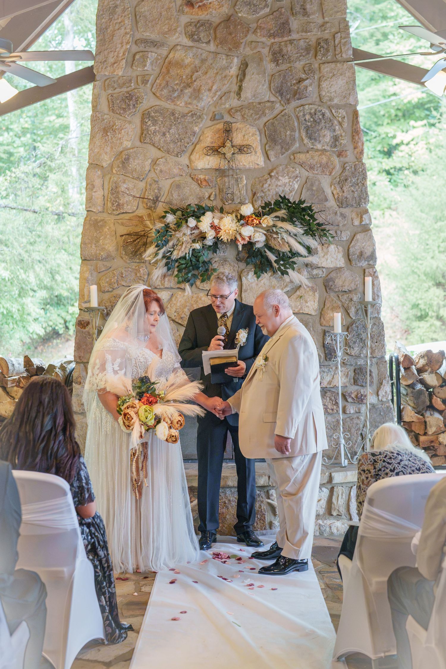 Bride and groom exchanging vows at elegant stone chapel wedding ceremony with floral arch and white aisle runner at the Roosevelt Lodge.