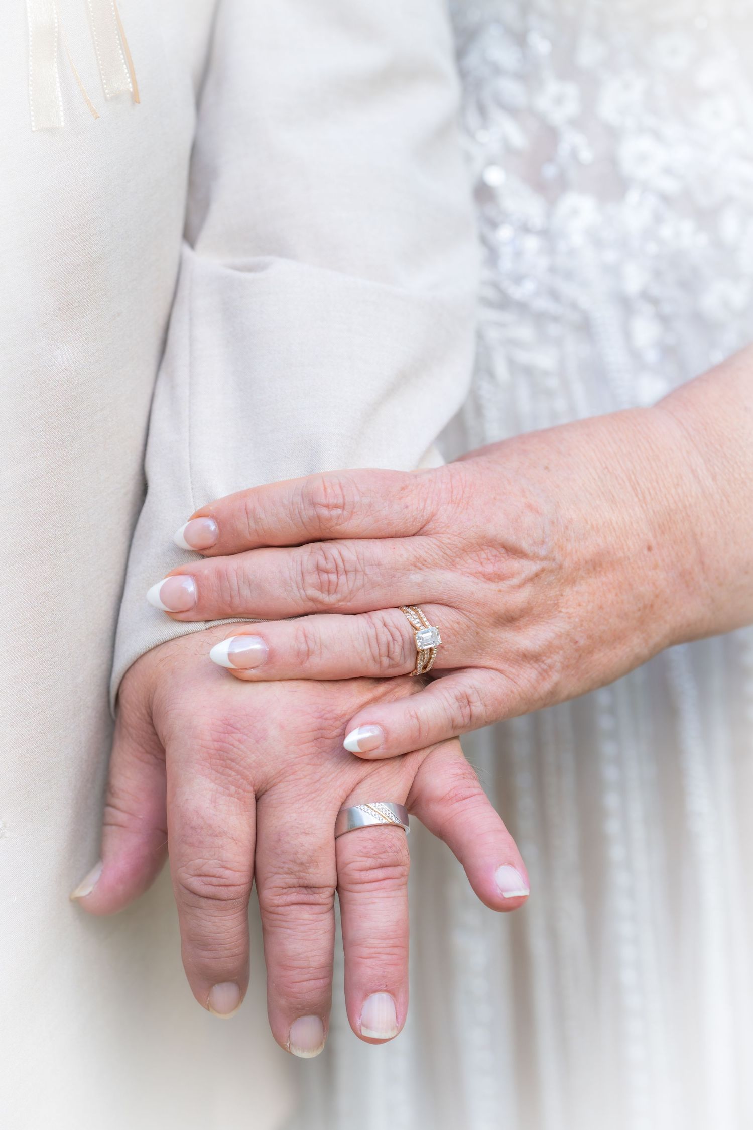 Close-up of couple's hands showing wedding rings, bride in white lace dress, symbolizing lasting love and marriage.