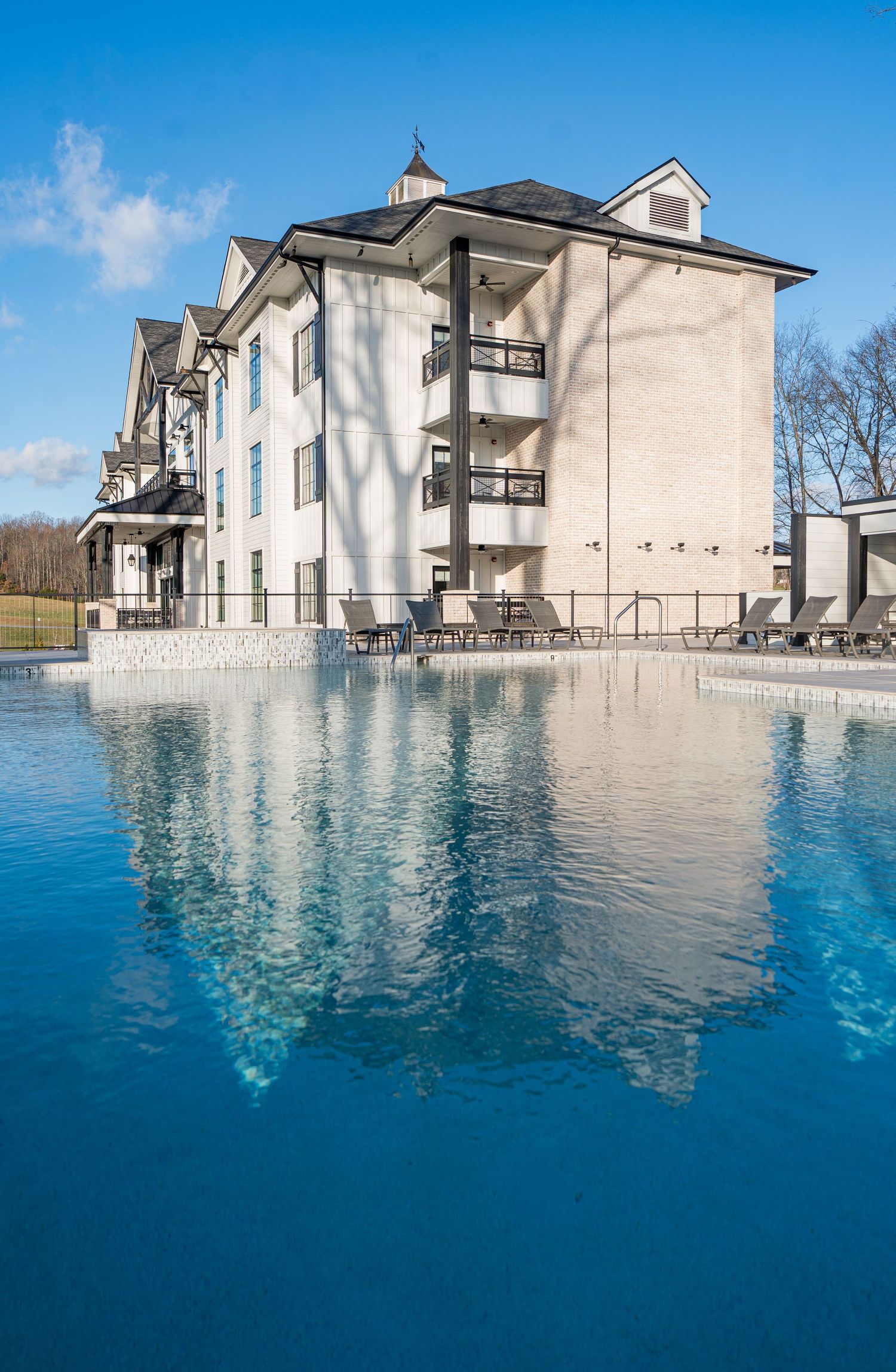 Luxury hotel with balconies reflecting in a crystal-clear outdoor pool under a bright blue sky.