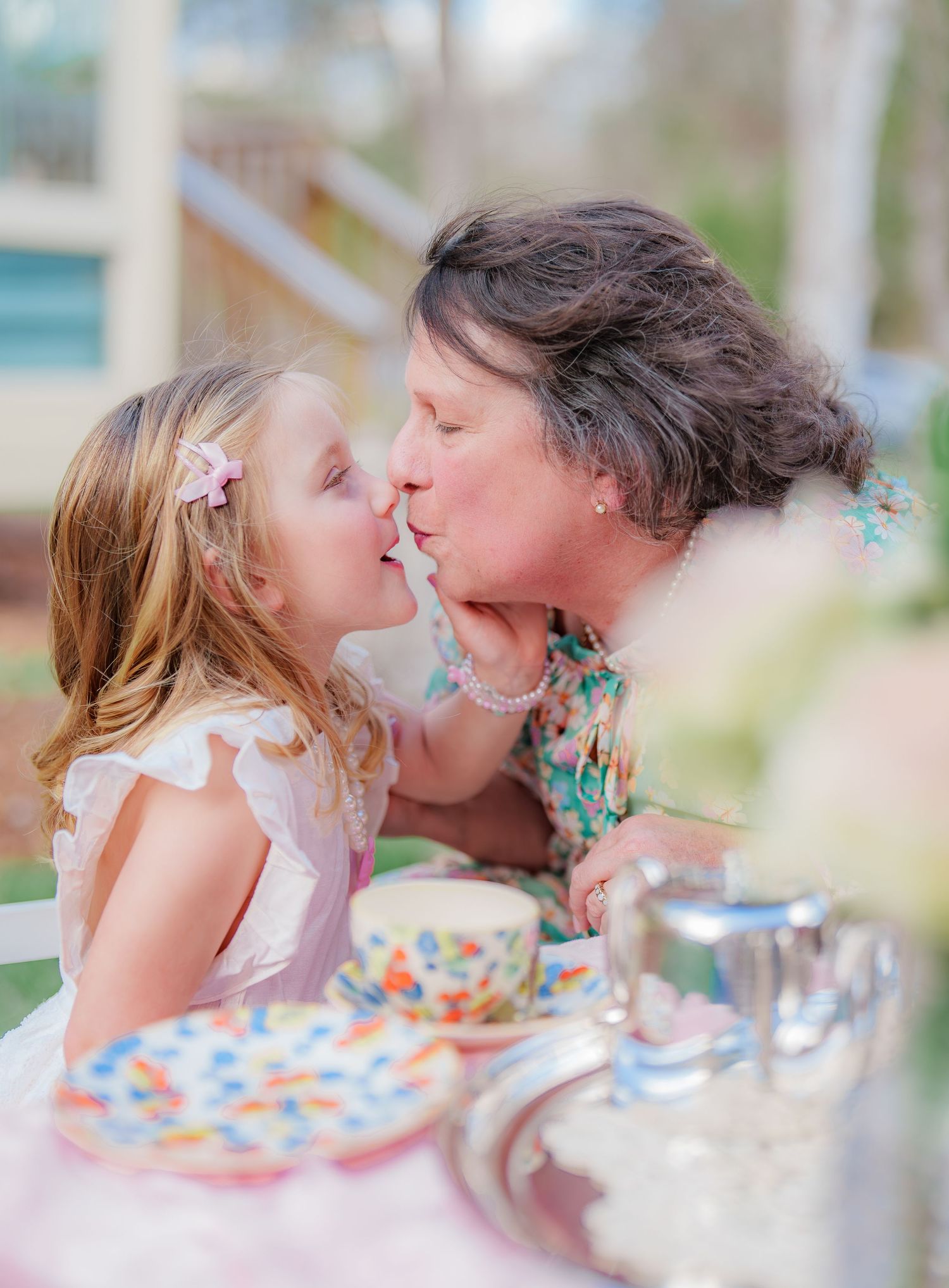 Grandmother and young girl sharing a sweet kiss at a colorful tea party table outdoors.