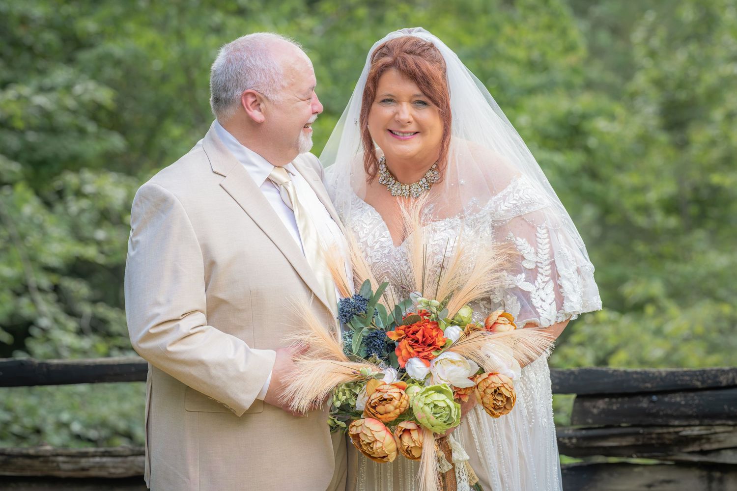 Bride and groom smiling together outdoors, bride wearing lace gown, veil, and holding a bouquet at the Roosevelt Lodge in Gatlinburg, TN.