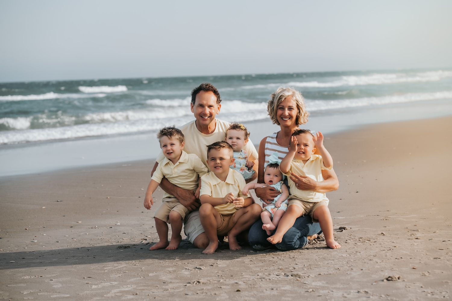 Family of seven poses together on a sandy beach with ocean waves in the background.
