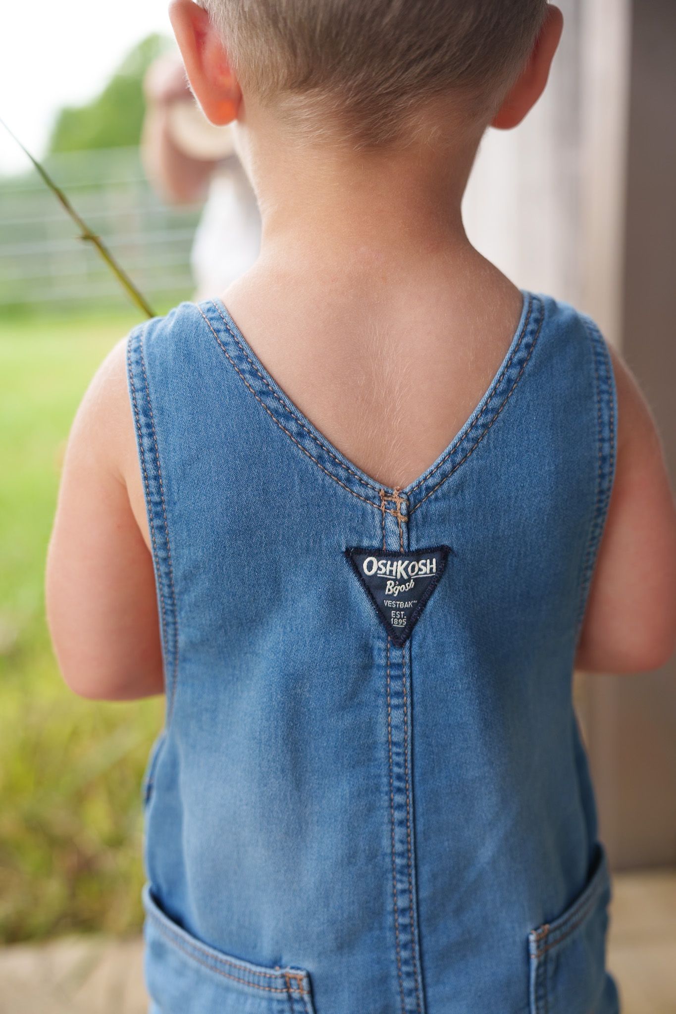 Close-up back view of young boy wearing OshKosh denim overalls outdoors.