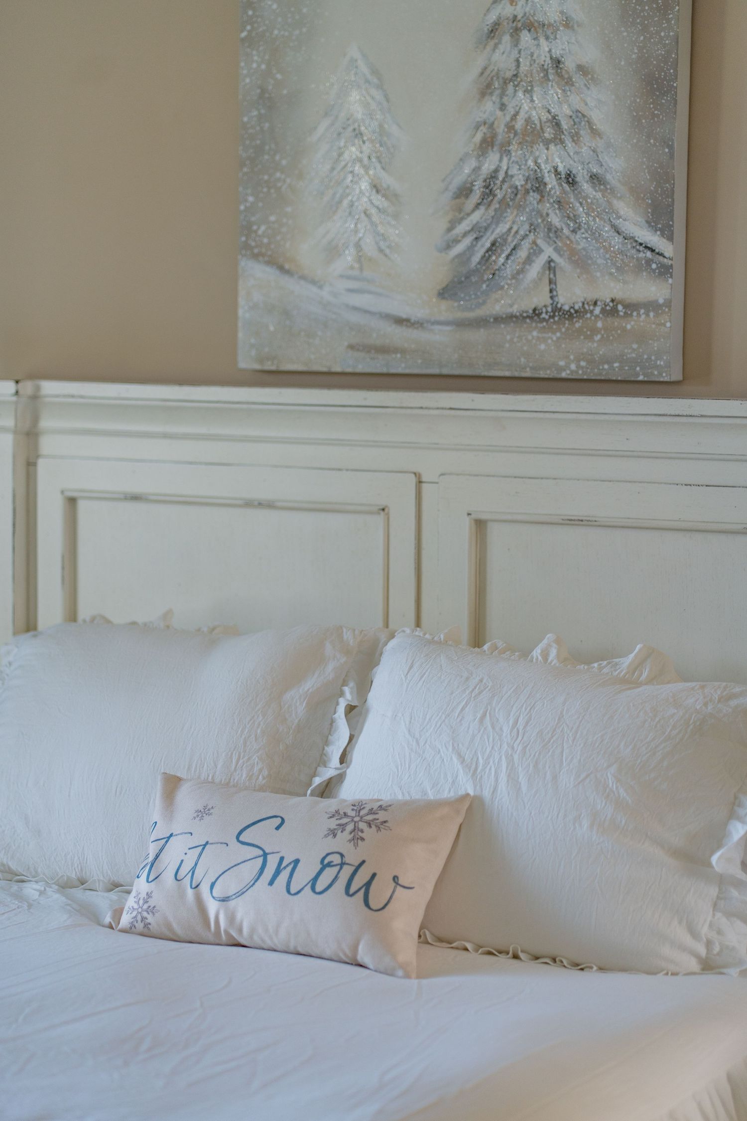 White bed with Let It Snow pillow, white headboard, and snowy Christmas tree painting above.