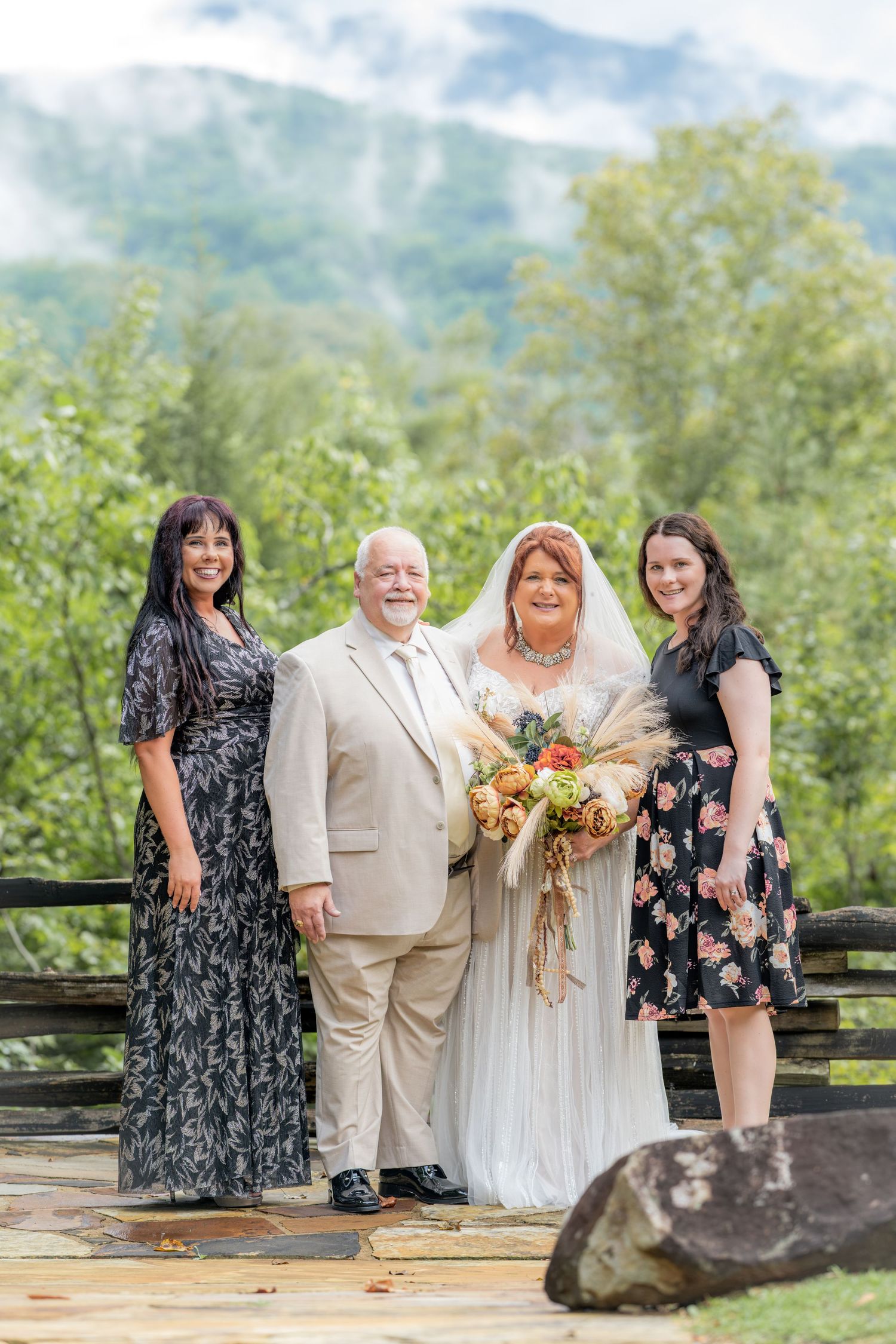 Bride and groom pose with two guests on a mountain wedding venue deck surrounded by lush green trees.